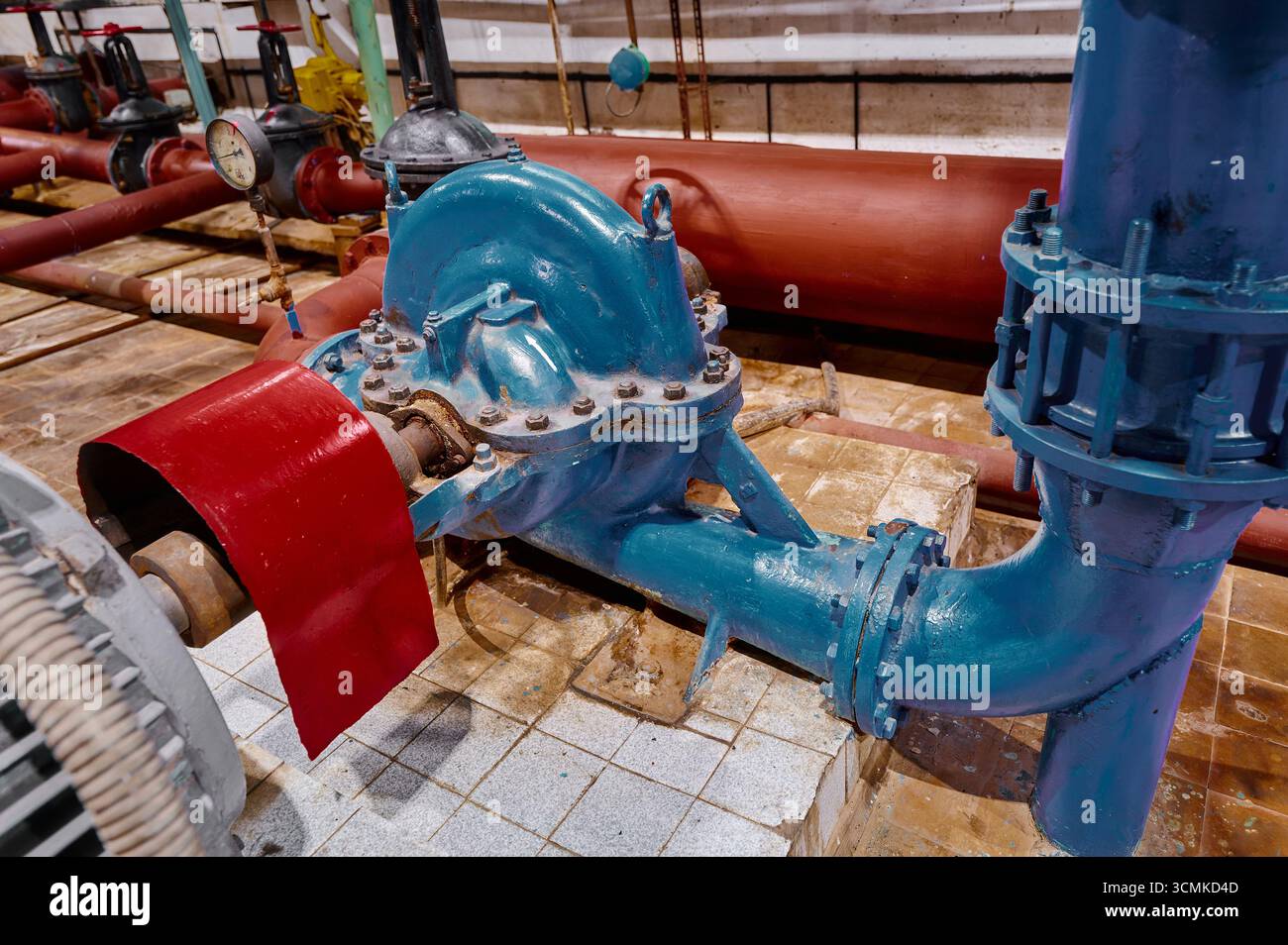 Système de pompe à eau industrielle fonctionnant dans une installation avec tuyauterie rouge et bleue pendant les heures de travail diurne Banque D'Images