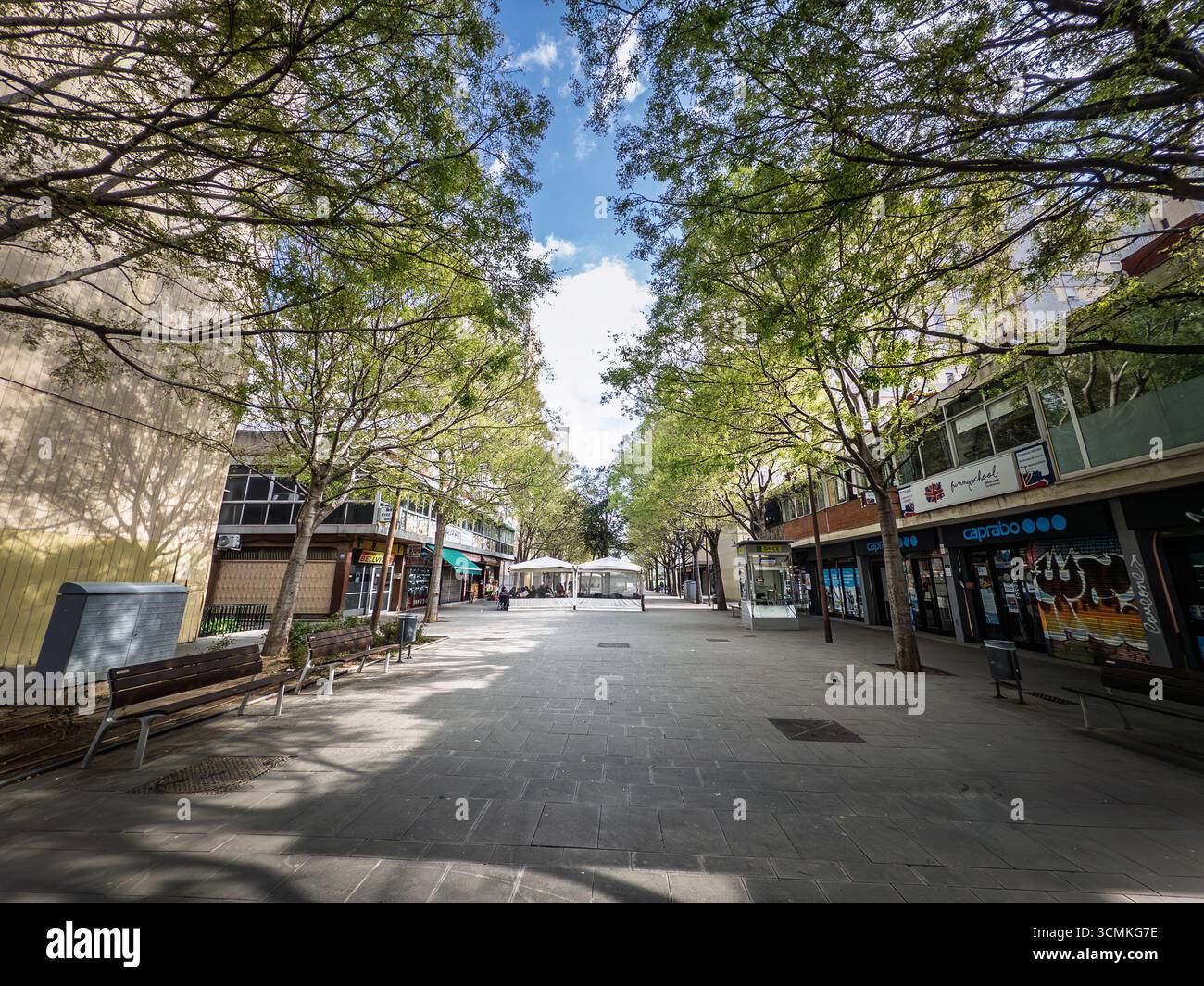 BARCELONE, ESPAGNE - 5 AVRIL 2025 : rue piétonne dans le centre de Bellvitge, Barcelone. Promenade bordée d'arbres et magasins locaux montre une voiture public sp Banque D'Images