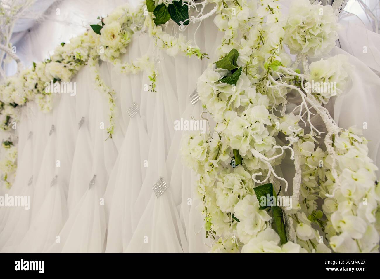 Cette élégante toile de fond de mariage présente des fleurs blanches luxuriantes entrelacées de délicate verdure sur un tissu doux et drapé. La configuration crée un romantique Banque D'Images