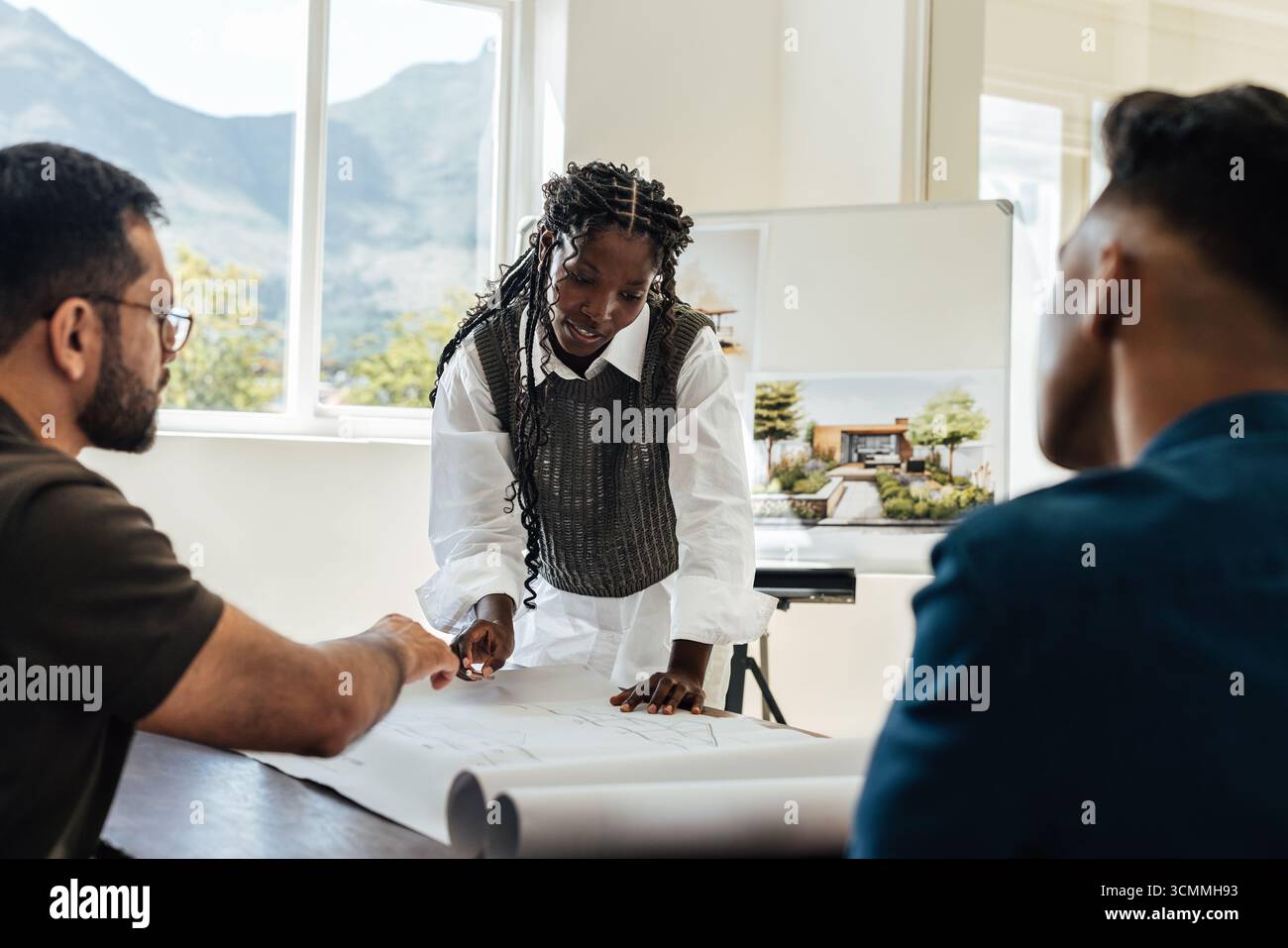 Trois personnes discutent des plans et des conceptions architecturales dans un espace de travail lumineux et moderne, mettant en valeur le travail d'équipe et la créativité. Banque D'Images