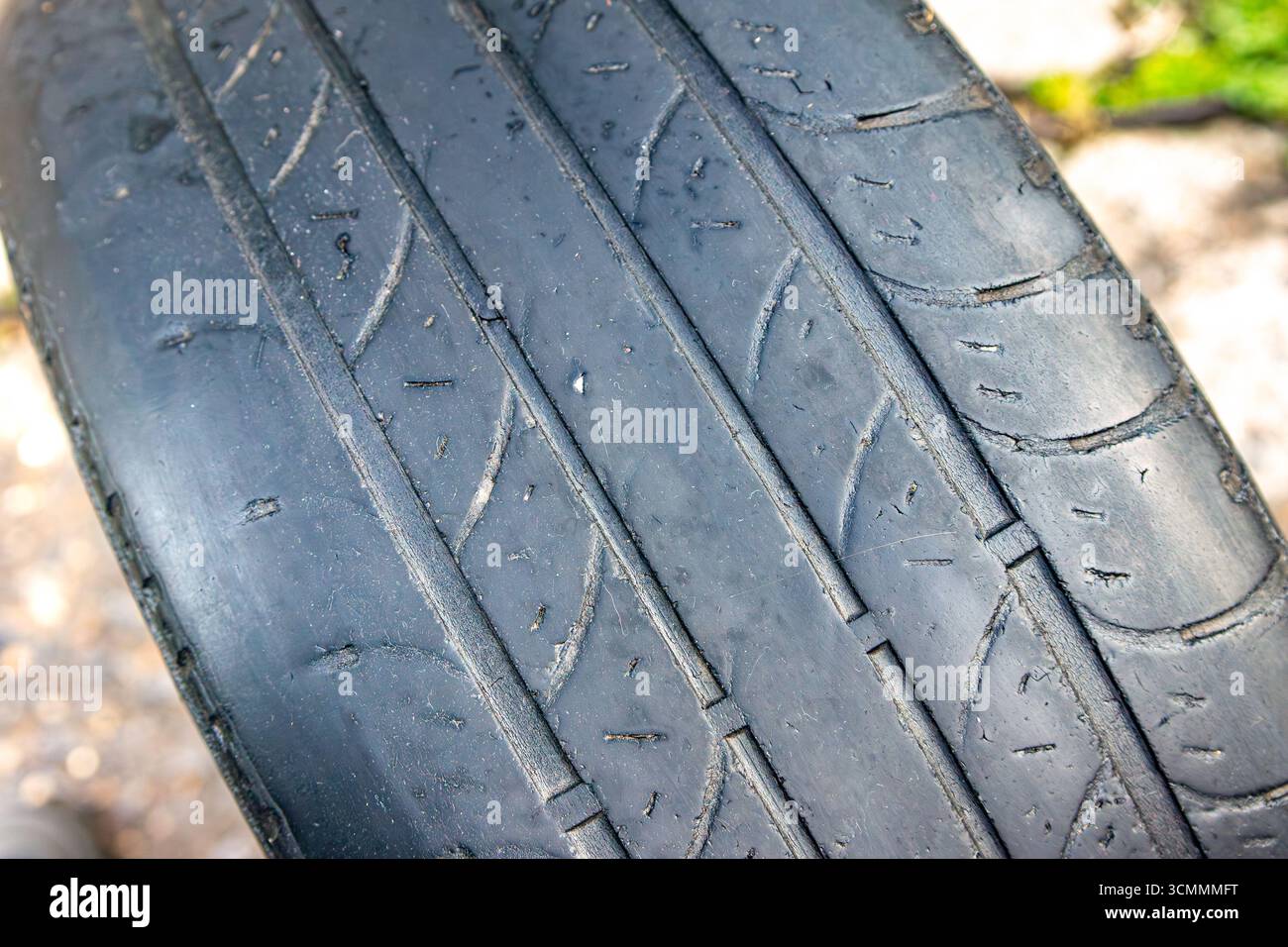 Gros plan d'un pneu très usé montrant l'usure de la bande de roulement, des fissures et des débris incrustés indiquant une dégradation structurelle et un risque potentiel de défaillance. avec s Banque D'Images