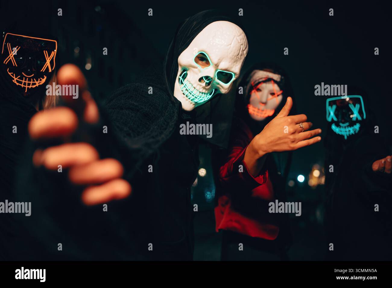 Un groupe d'individus portant des masques lumineux, posant dans une ville au milieu d'une ambiance sombre et sombre, créant un visuel intrigant et atmosphérique avec v Banque D'Images