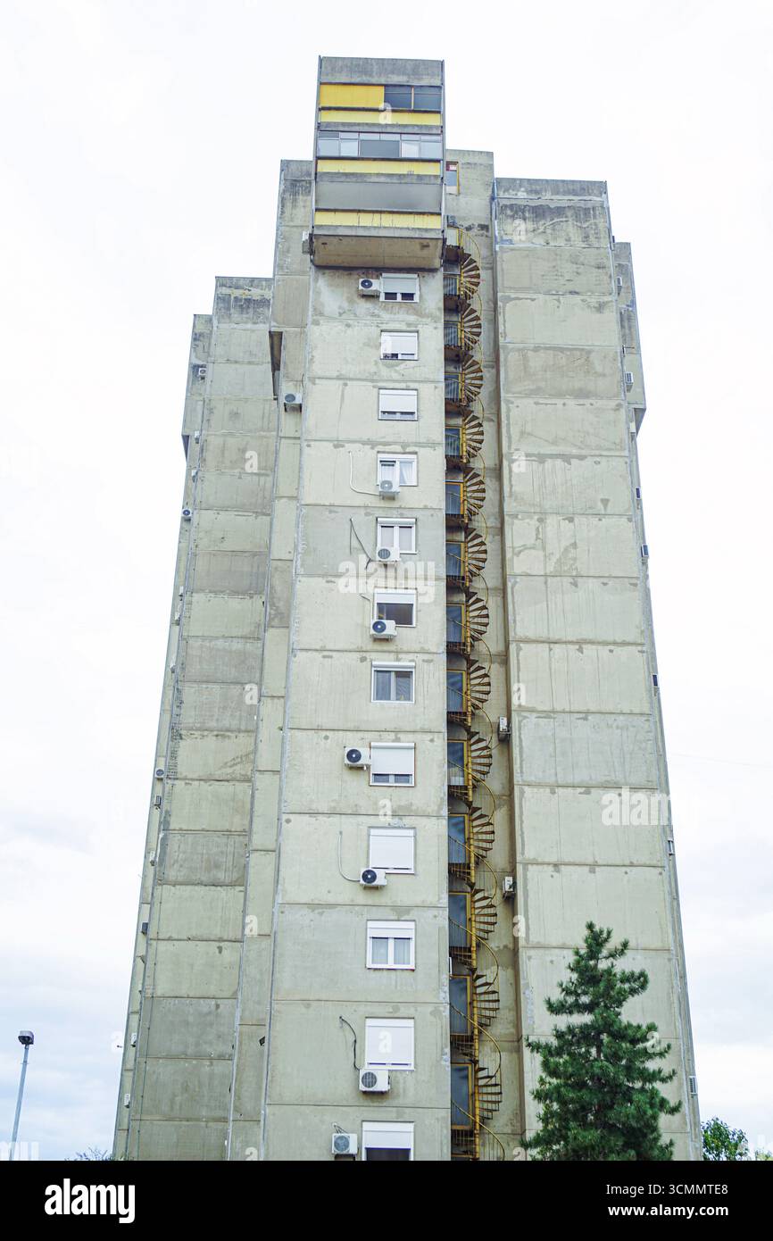 Une photo verticale de la façade latérale d'un grand immeuble dans le style Bratlism : un mur de béton gris avec des fenêtres et un escalier de feu en spirale Banque D'Images