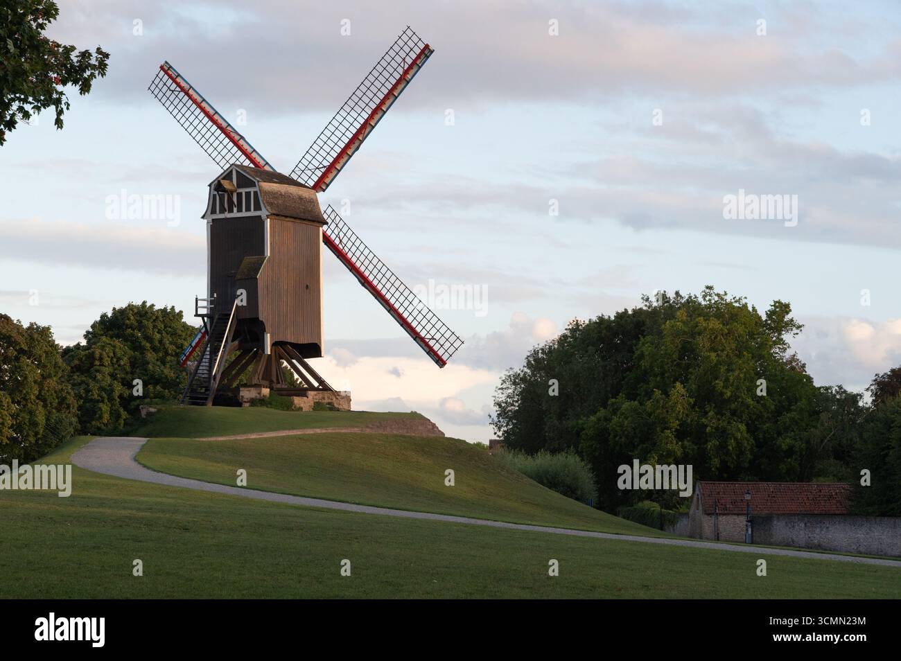 Un moulin à vent pittoresque se dresse majestueusement sur une colline, embrassé par une verdure vibrante et un ciel serein. Banque D'Images