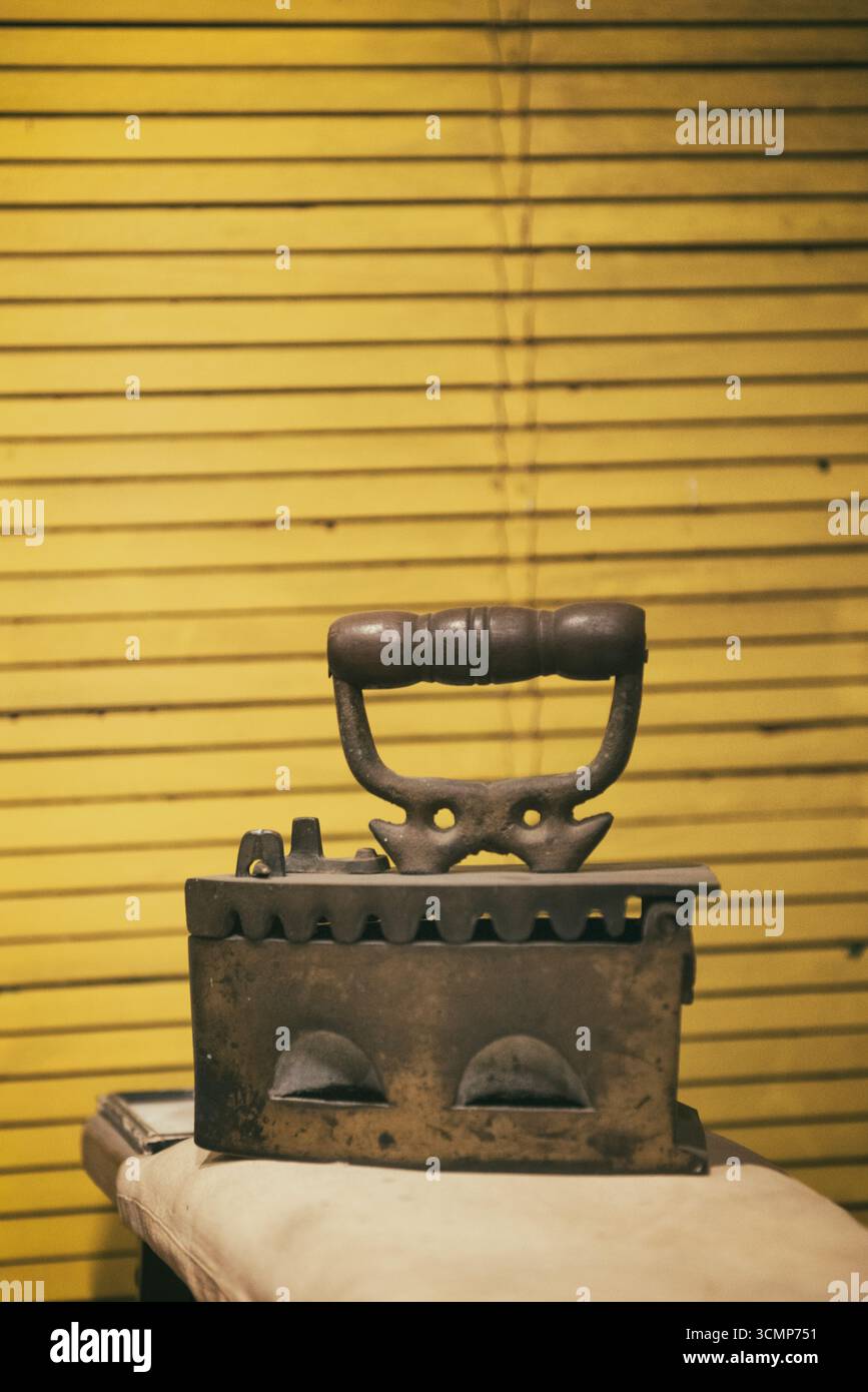 Un fer Vintage repose sur une planche à repasser, une relique nostalgique sur un fond jaune éclatant Banque D'Images