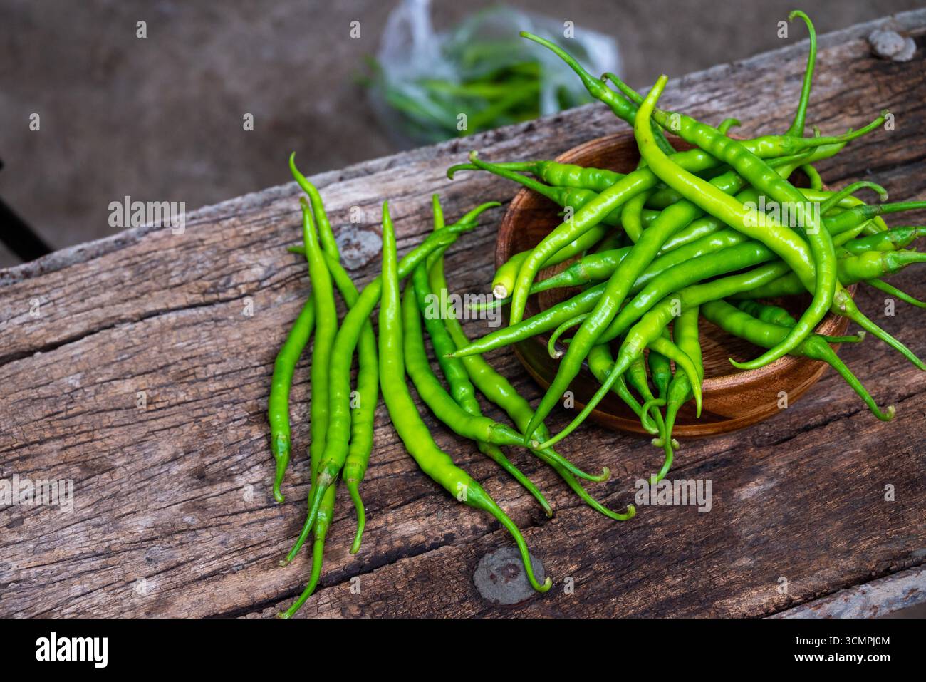 Piments verts bio frais placés dans un bol en bois avec un peu dispersé autour sur une surface en bois rustique. Banque D'Images