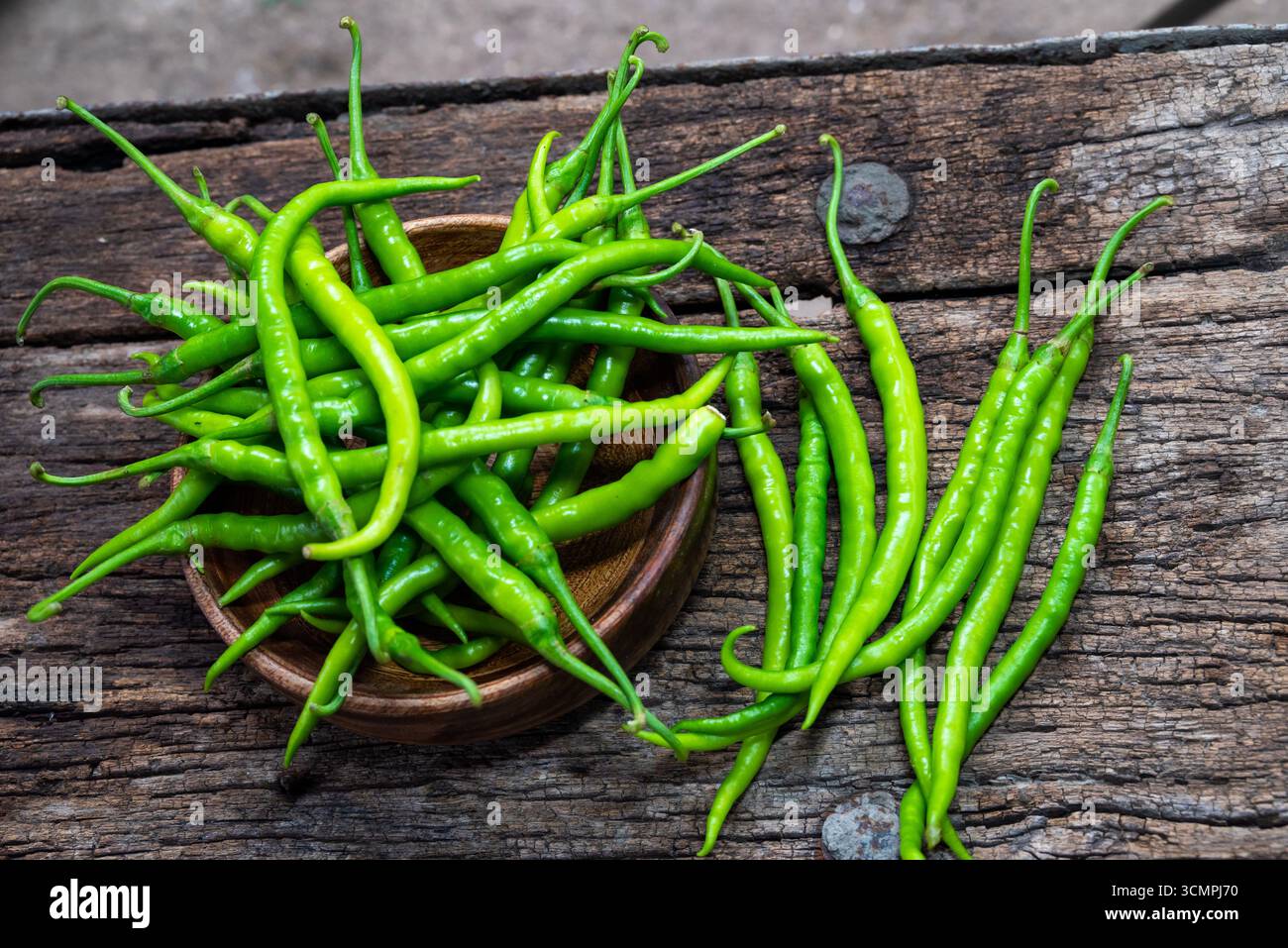 Piments verts bio frais placés dans un bol en bois avec un peu dispersé autour sur une surface en bois rustique. Banque D'Images