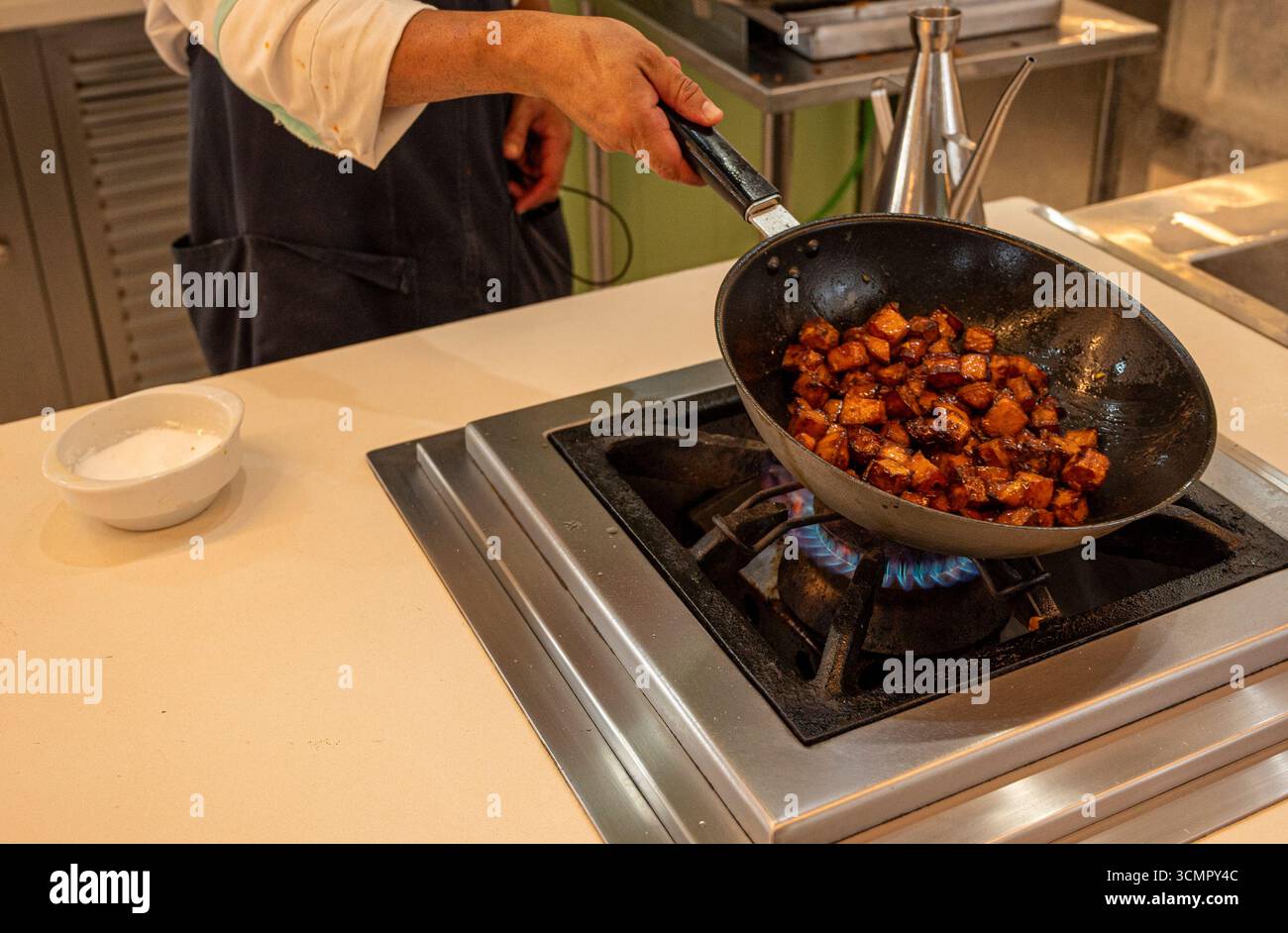 Un chef cuisinier fait cuire des aliments dans une casserole sur une cuisinière. La poêle est remplie de viande et de légumes Banque D'Images