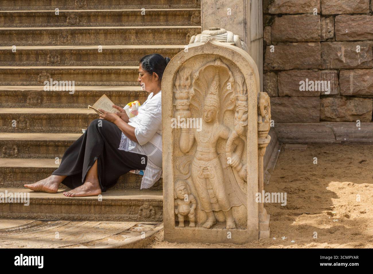 Sri Lanka - Anuradhapura - Temple Steps - femme lisant sur des escaliers en pierre sculptée Banque D'Images