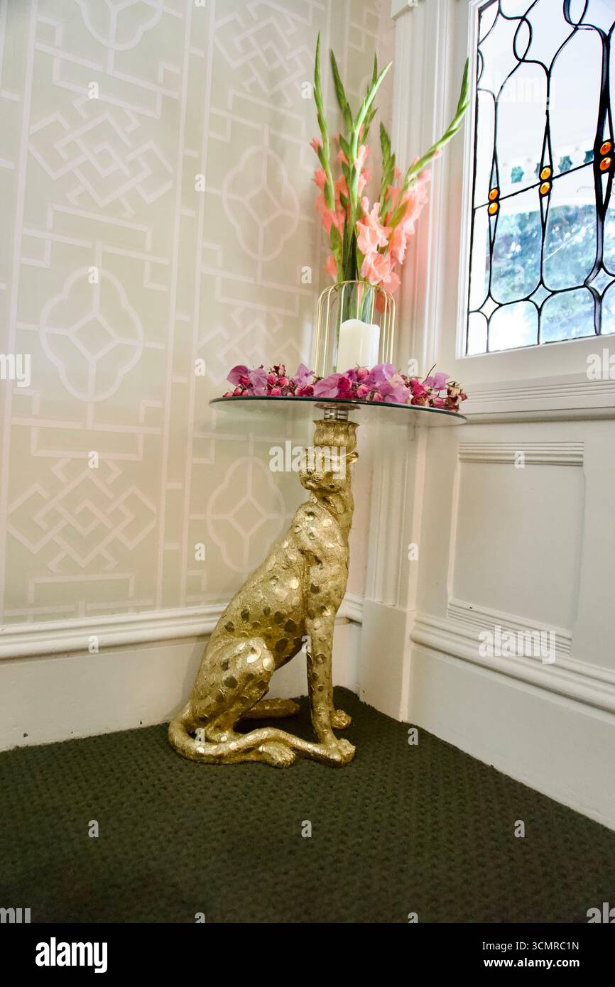 Table d'appoint guépard dorée avec fleurs et bougie près d'un vitrail Banque D'Images Table d'appoint guépard dorée avec fleurs et bougie près d'un vitrail Banque D'Images