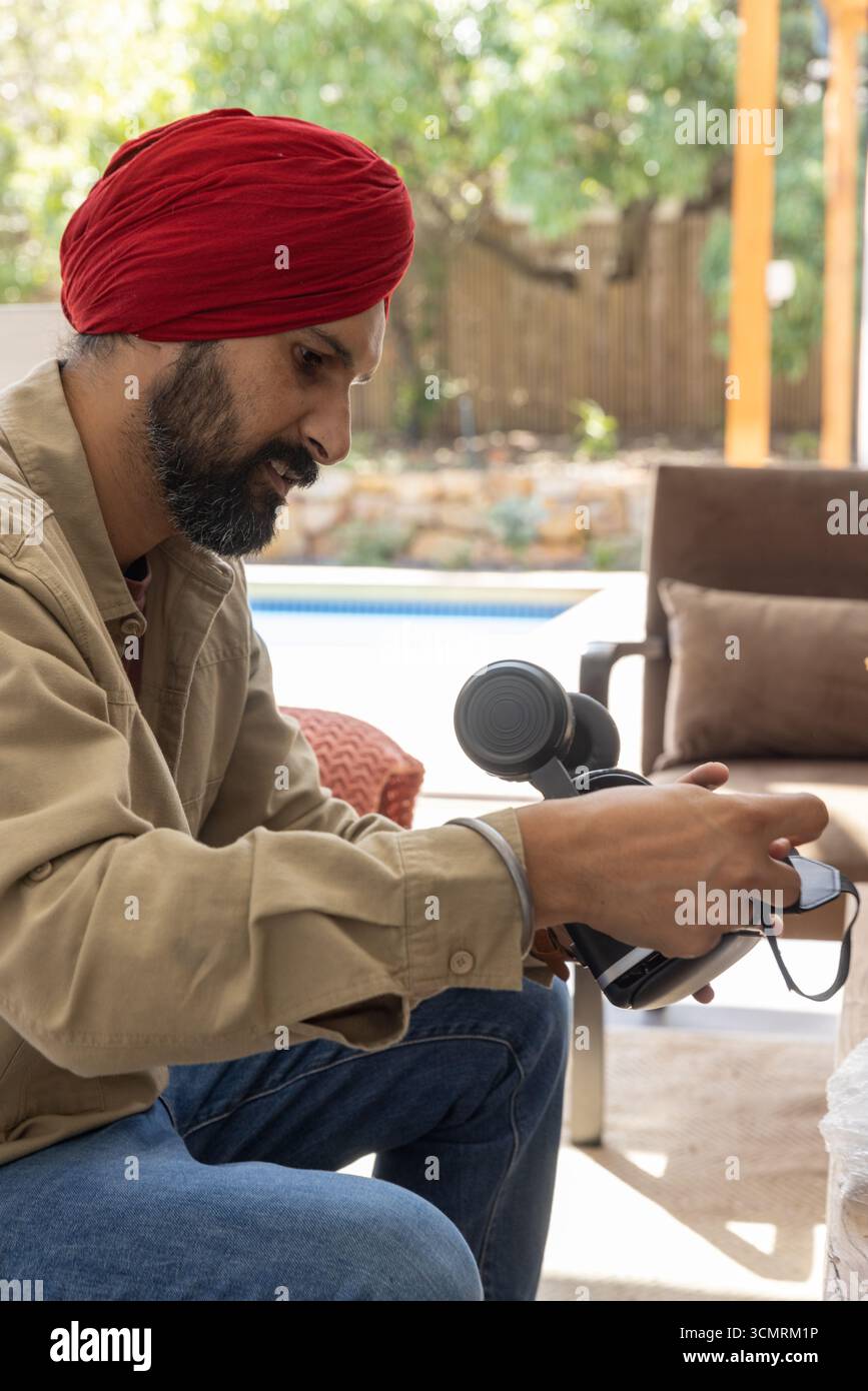 Homme indien assis sur une chaise longue sur le patio près de la piscine tenant le dispositif de casque vr Banque D'Images