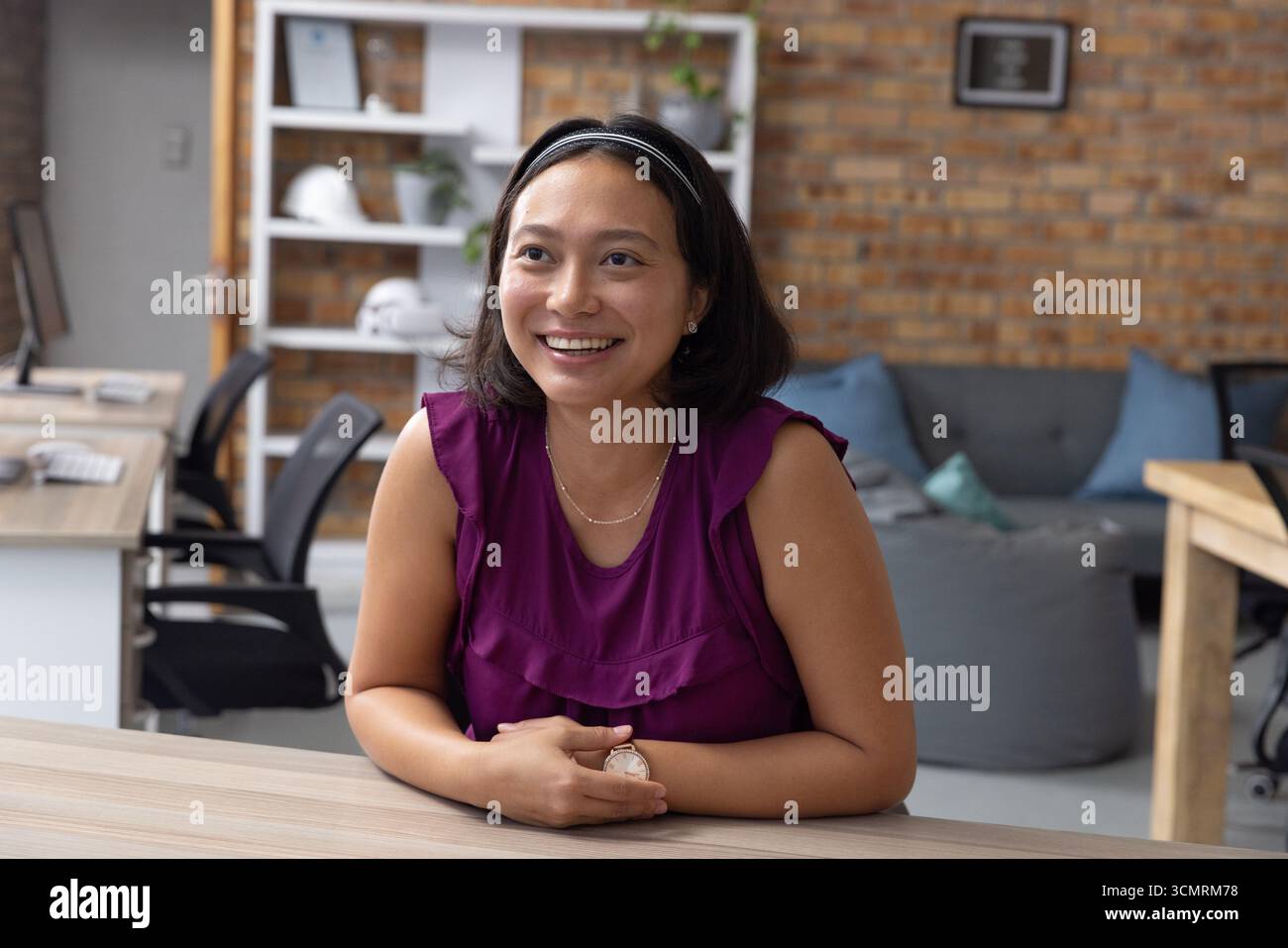 Femme asiatique tapant sur le clavier au bureau en bois dans le bureau avec des casques de sécurité et des plantes Banque D'Images