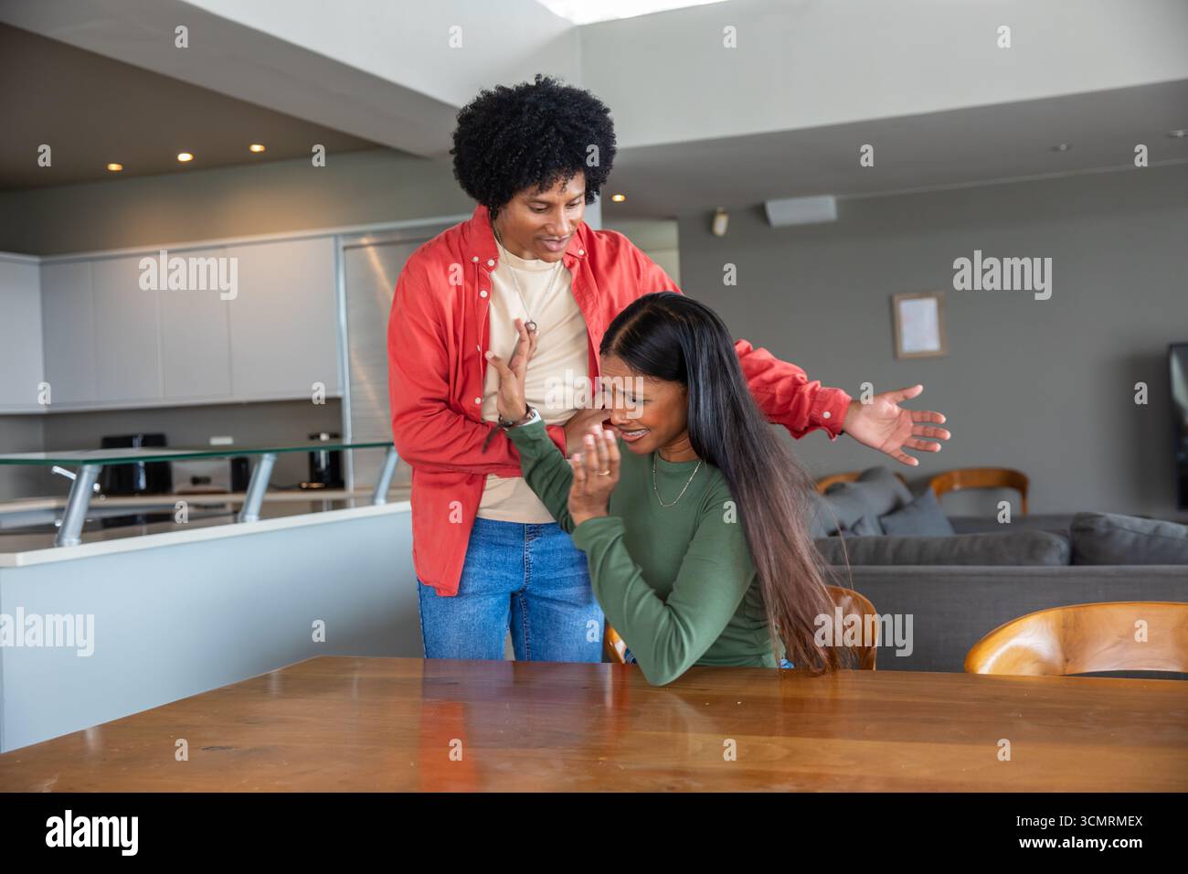 Couple diversifié consolant et essuyant les larmes à la cuisine ouverte moderne avec table à manger Banque D'Images Couple diversifié consolant et essuyant les larmes à la cuisine ouverte moderne avec table à manger Banque D'Images