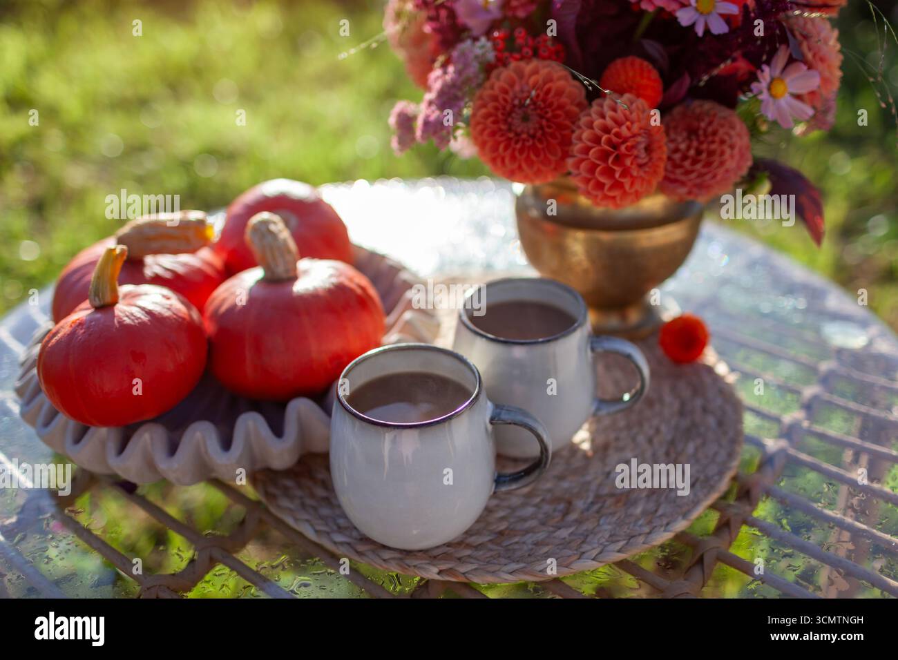 Gros plan de boissons chaudes au café dans des tasses pour le petit déjeuner dans le jardin d'automne. Table décorée avec arrangement de fleurs de dahlia et citrouilles pour l'automne en orange Banque D'Images