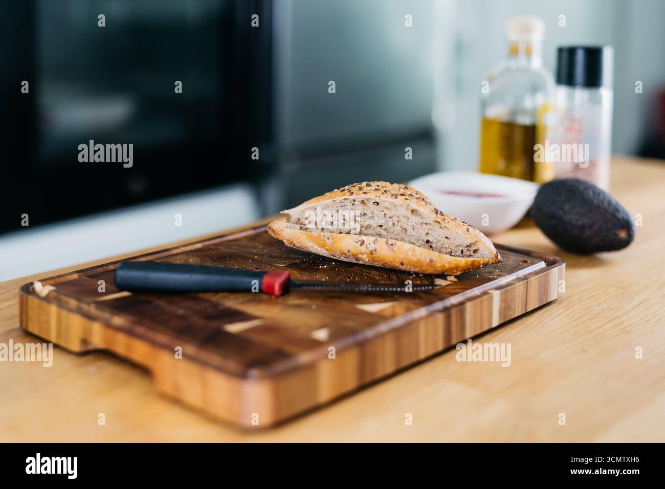 Le pain artisanal repose sur une planche à découper en bois, avec de l'huile d'olive, des épices et de l'avocat à proximité, créant une scène vibrante de préparation culinaire et de santé Banque D'Images