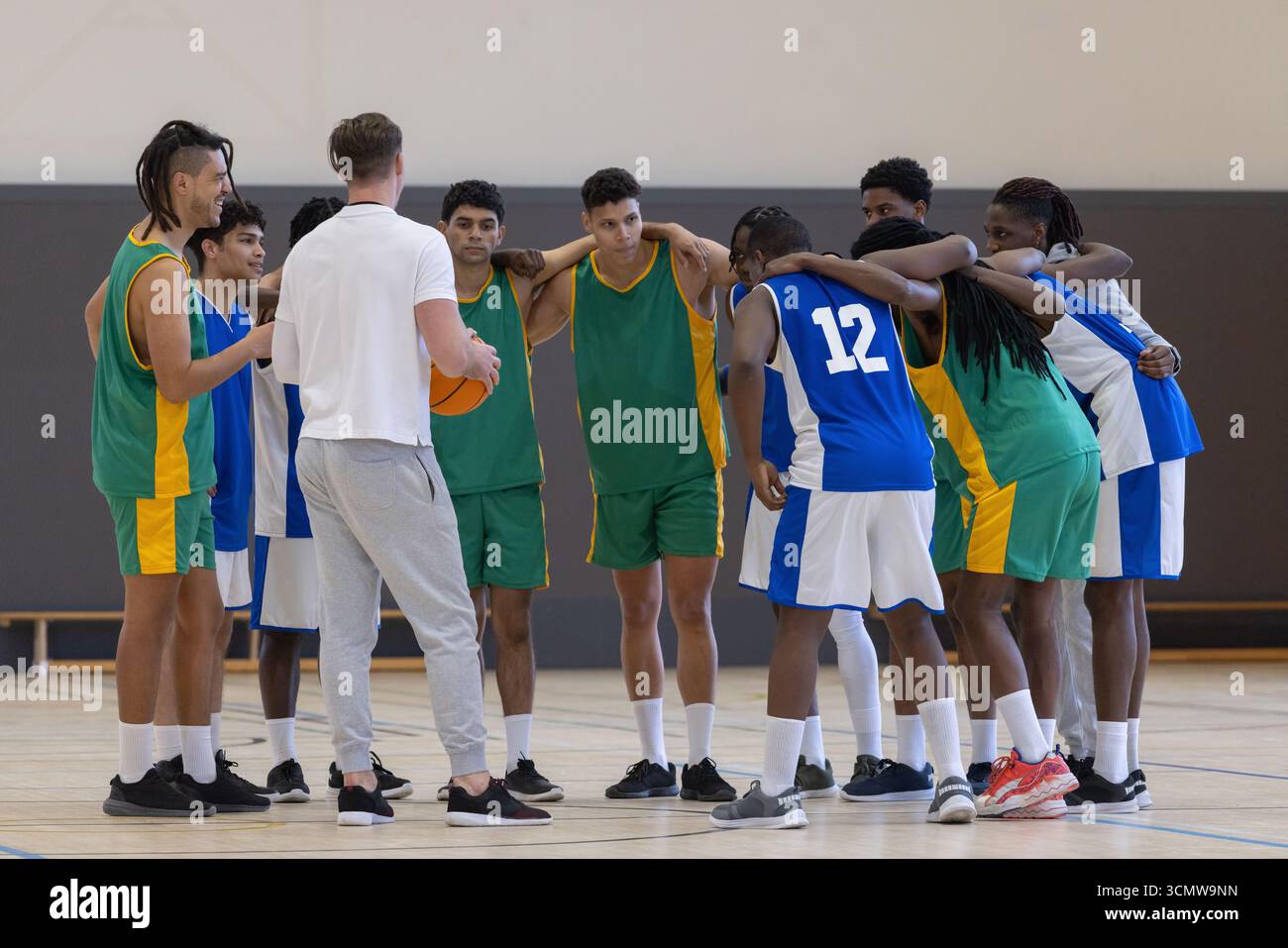 Équipe masculine de basket-ball diversifiée se blottissant autour de l'entraîneur qui tient des matchs de basket-ball sur un terrain en bois poli Banque D'Images
