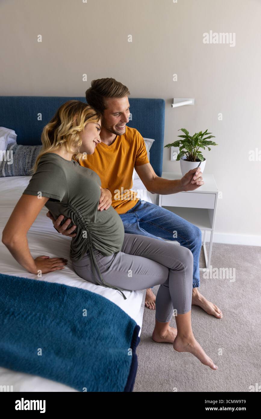 Couple berçant la bosse de bébé tout en prenant selfie smartphone sur le lit avec couverture bleue Banque D'Images