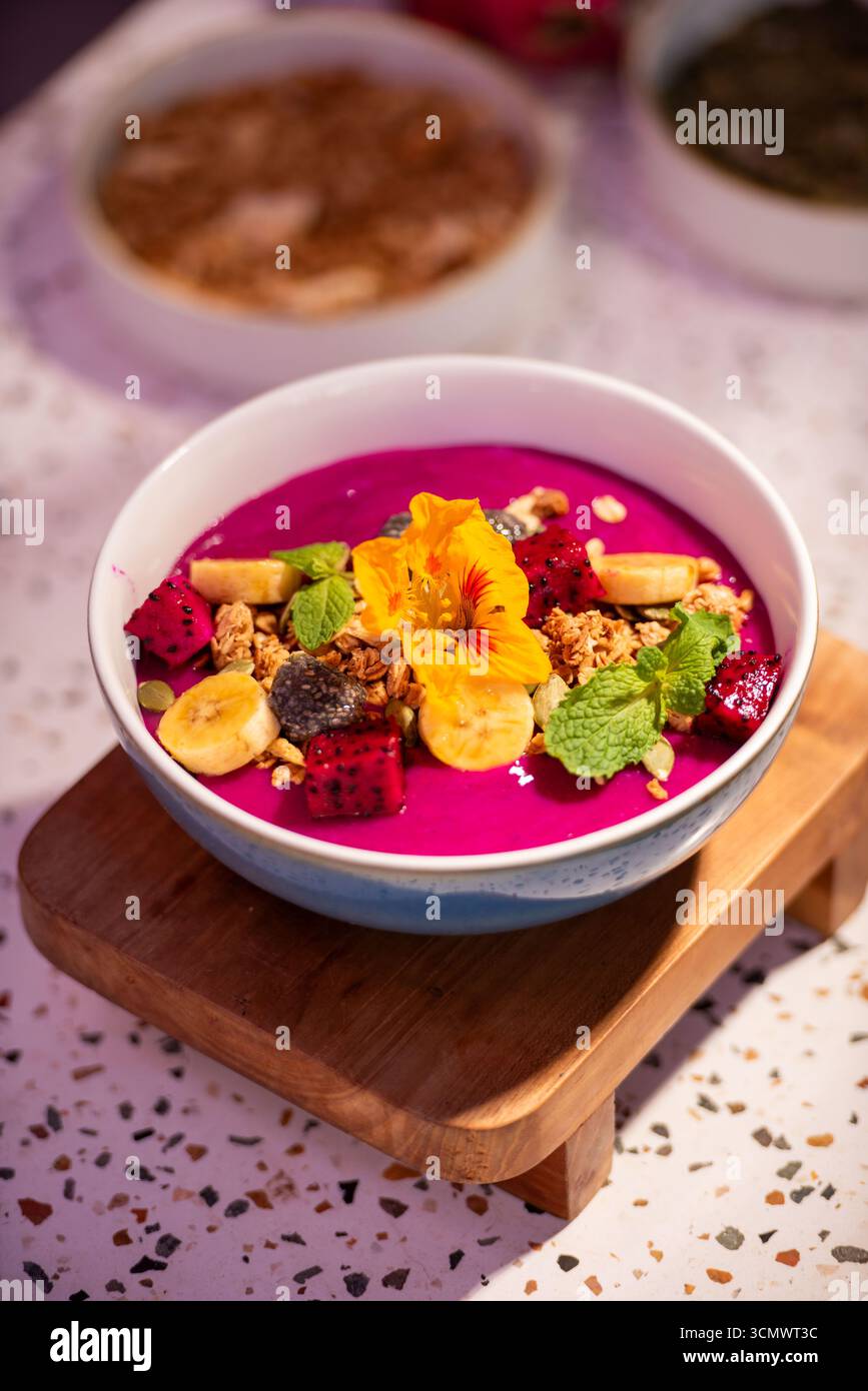 Bol coloré à smoothie aux fruits du dragon avec banane, granola, fleur comestible et feuilles de menthe fraîche. Concept de petit déjeuner sain avec des fruits tropicaux vibrants Banque D'Images