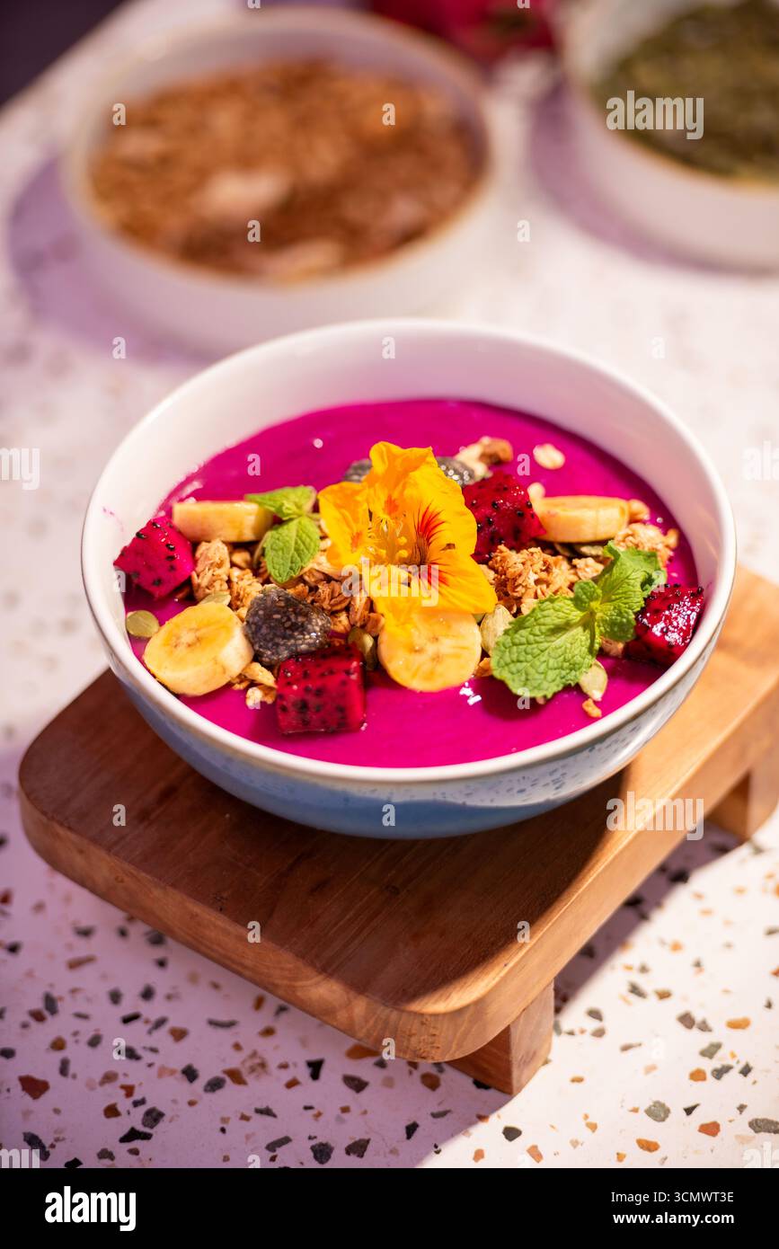 Bol coloré à smoothie aux fruits du dragon avec banane, granola, fleur comestible et feuilles de menthe fraîche. Concept de petit déjeuner sain avec des fruits tropicaux vibrants Banque D'Images