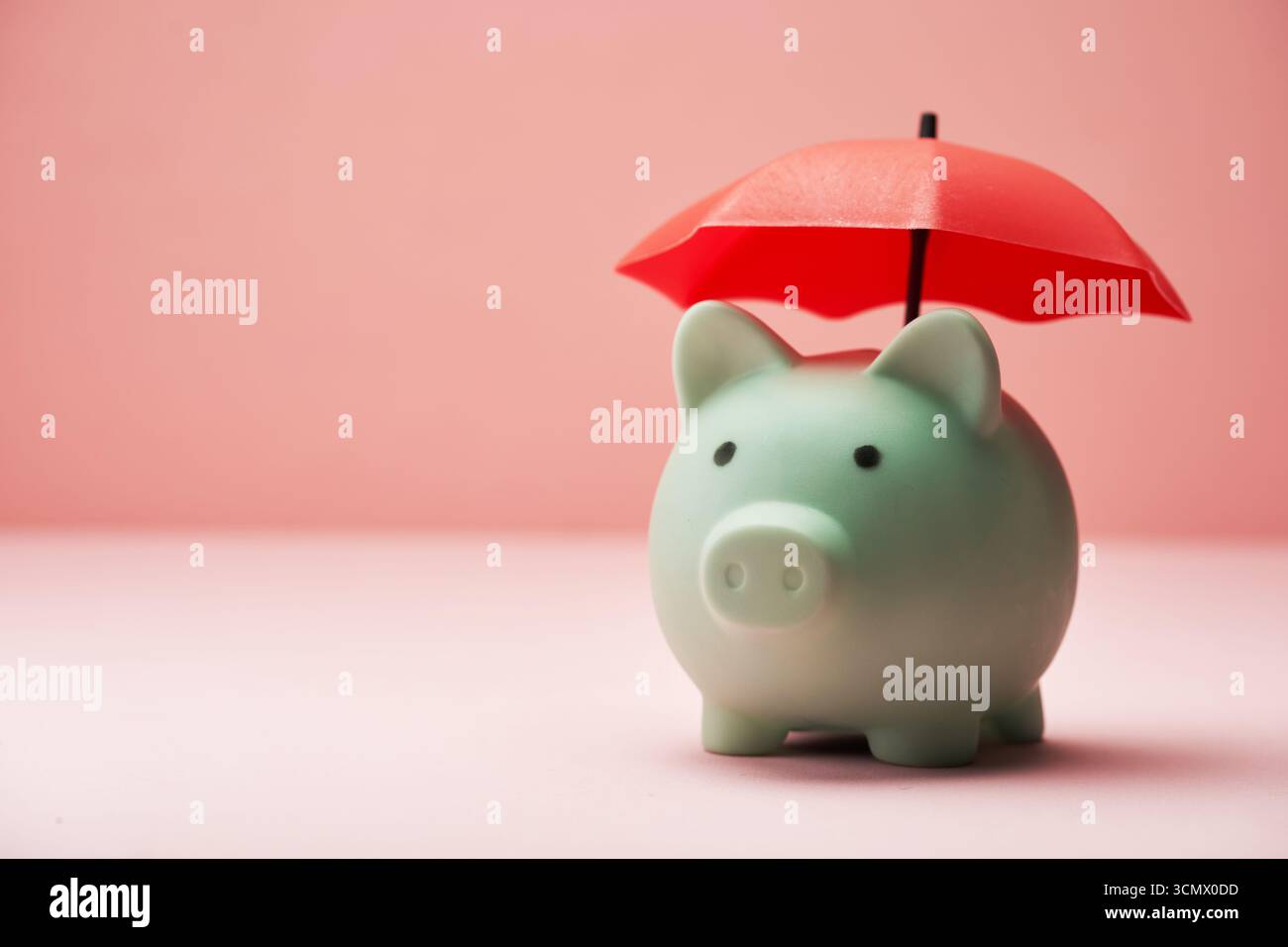 Tirelire bleue sous parapluie rouge sur fond rose. Banque D'Images