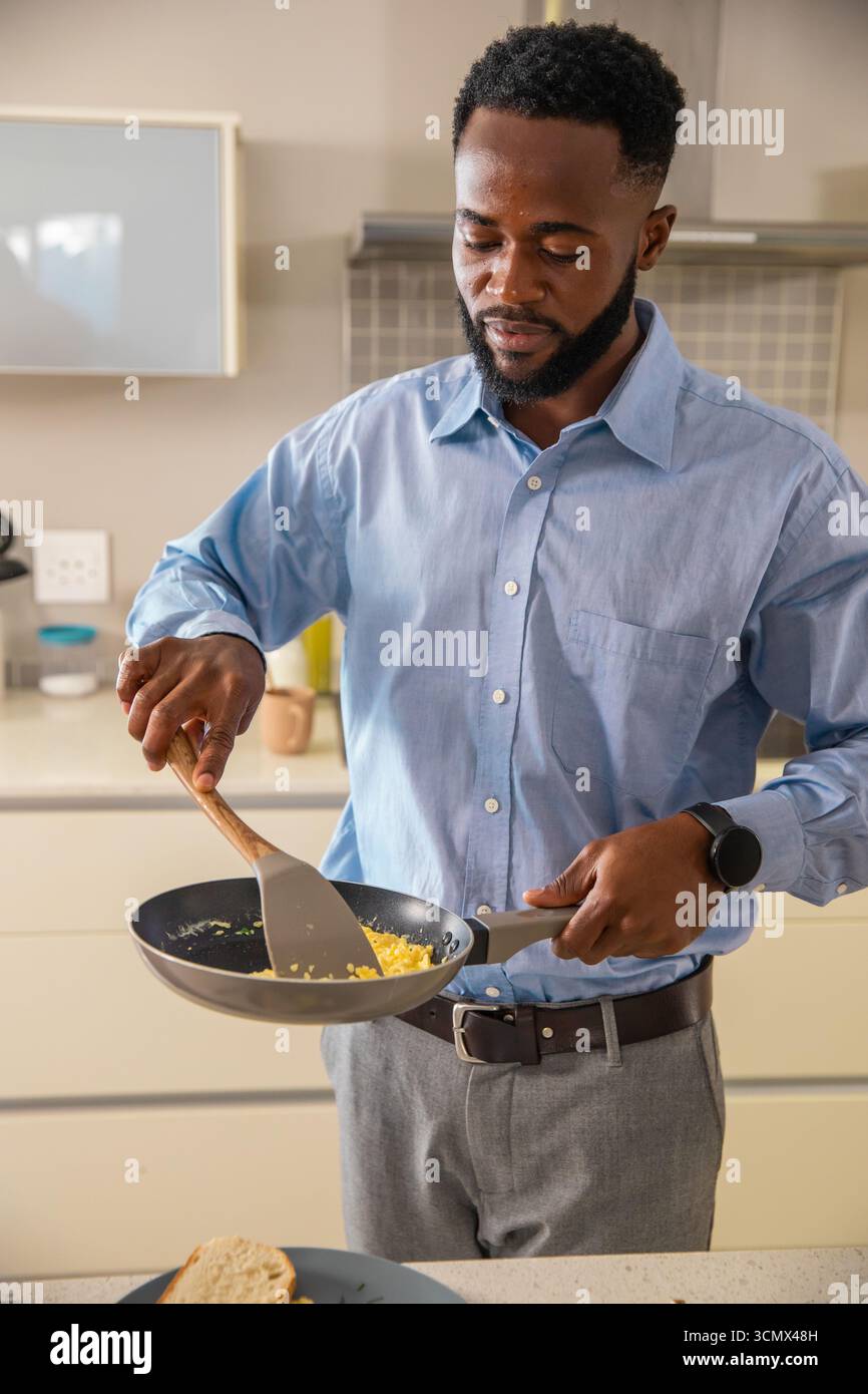 Homme afro-américain cuisinant des œufs brouillés dans une poêle à frire à l'aide d'une spatule dans la cuisine domestique Banque D'Images