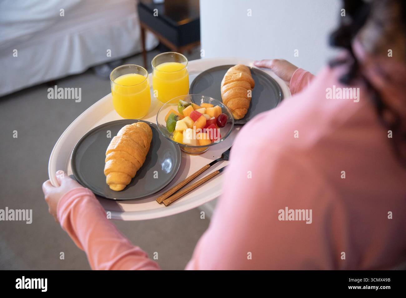 Femme adulte avec les cheveux bouclés avec plateau blanc sur le lit avec des croissants, bol de fruits, jus d'orange Banque D'Images Femme adulte avec les cheveux bouclés avec plateau blanc sur le lit avec des croissants, bol de fruits, jus d'orange Banque D'Images