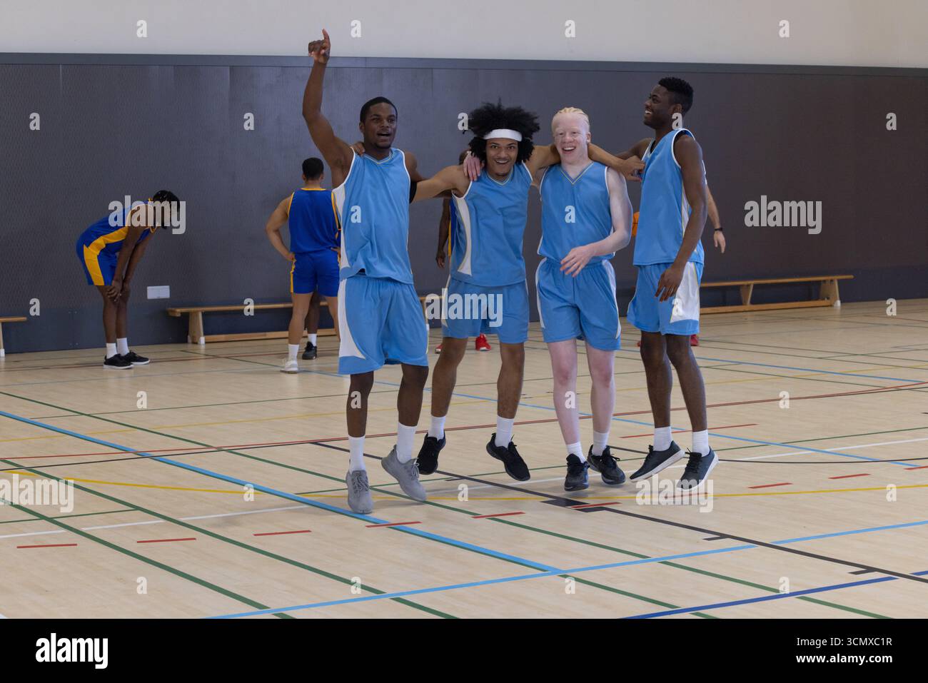 Divers coéquipiers masculins de basket-ball en uniforme acclamant et criant sur le terrain de gymnastique avec des lignes Banque D'Images