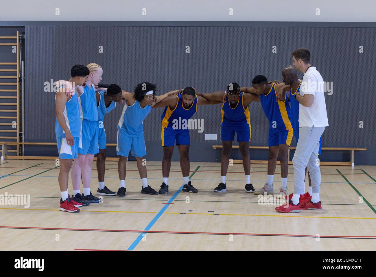 Équipe masculine diversifiée de basket-ball se blottissant autour de l'entraîneur sur le terrain avec des maillots Banque D'Images