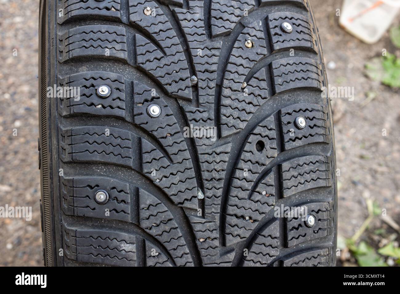 Gros plan d'un pneu d'hiver clouté montrant des goujons d'origine posés en usine, des goujons métalliques récemment remplacés et un trou vide pour goujon indiquant une perte pendant Banque D'Images