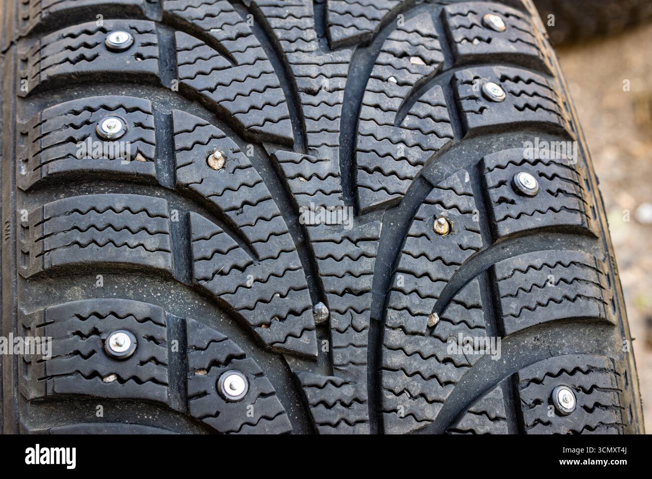 Gros plan d'un pneu d'hiver montrant à la fois des pointes métalliques neuves et anciennes, certaines tordues ou desserrées, suggérant qu'elles ont été mal mises en place avec un accent sélectif sur le th Banque D'Images
