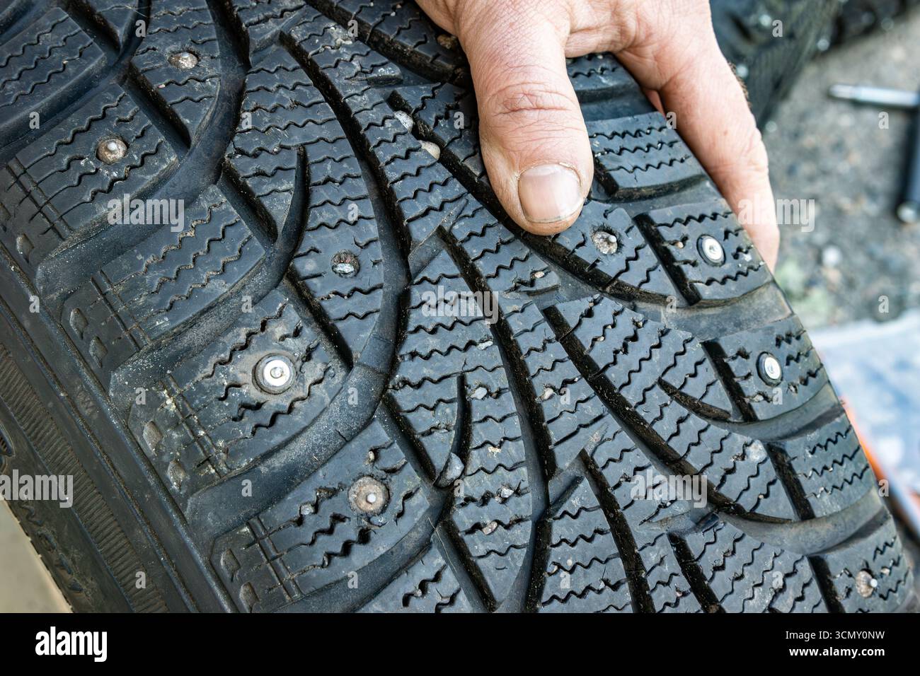 Gros plan d'un pneu d'hiver clouté montrant de petites pierres coincées dans les rainures de la bande de roulement et des trous vides pour les goujons, indiquant une usure et un risque de pression inégale Banque D'Images