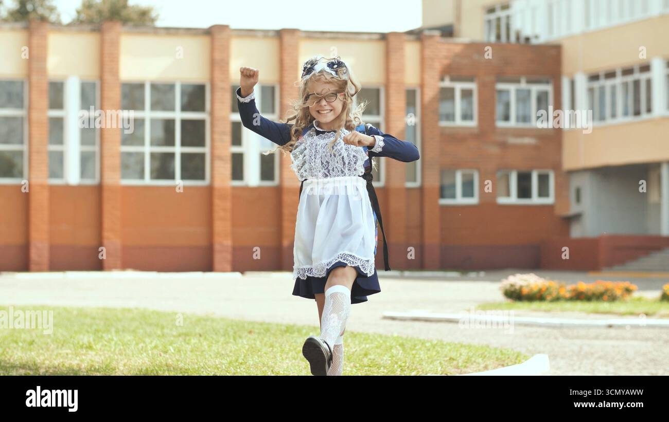 Heureuse écolière dansant devant le bâtiment de l'école, profitant de son éducation et de sa réussite scolaire Banque D'Images