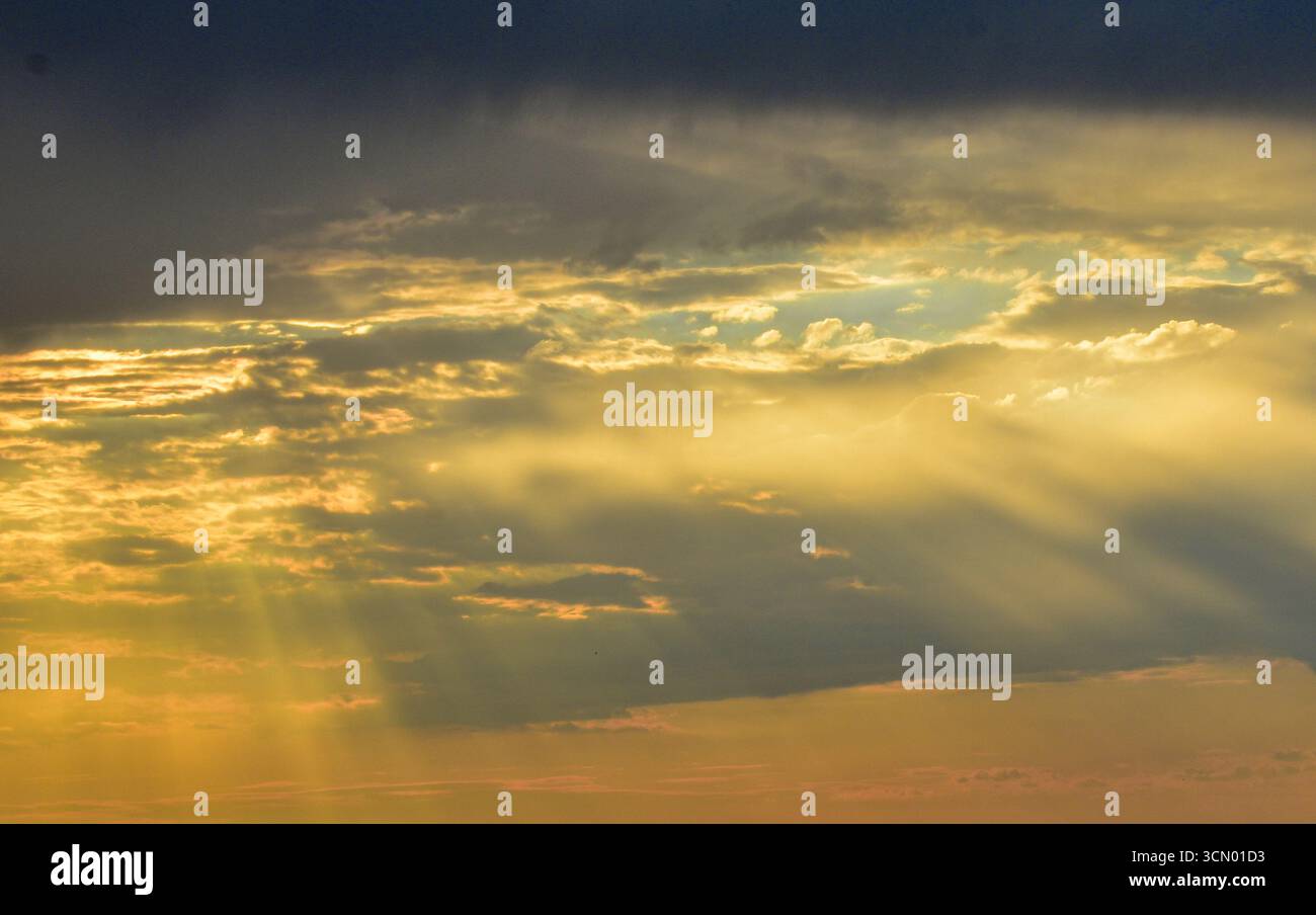 Coucher de soleil caché derrière des nuages brillants, éclairant le ciel dans des pastels délicats et ardents, mélangeant magie, douceur et intensité ensemble. Banque D'Images