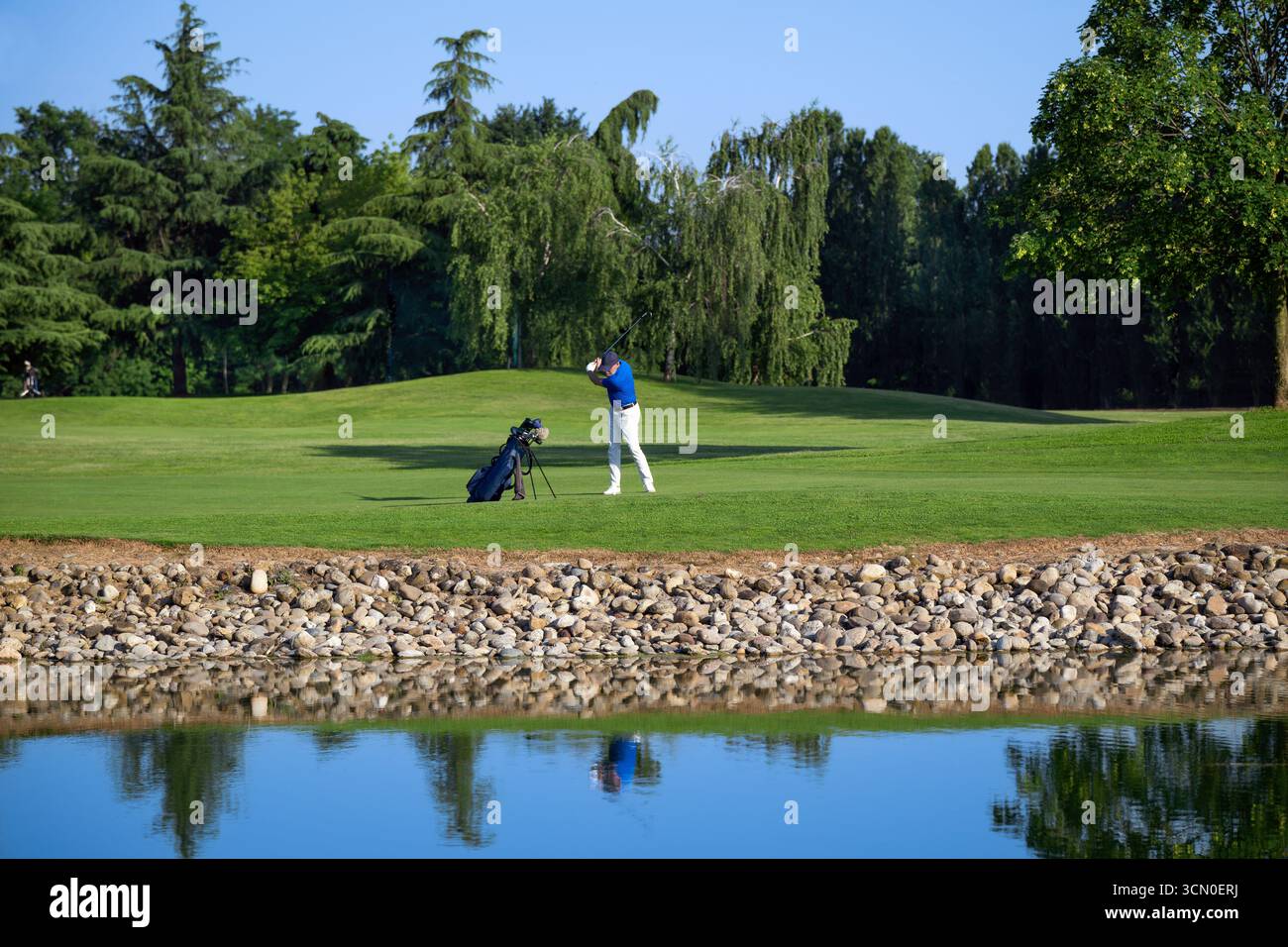 Golfeur frappant la balle de golf sur un beau parcours près de danger d'eau, se reflétant dans l'eau Banque D'Images