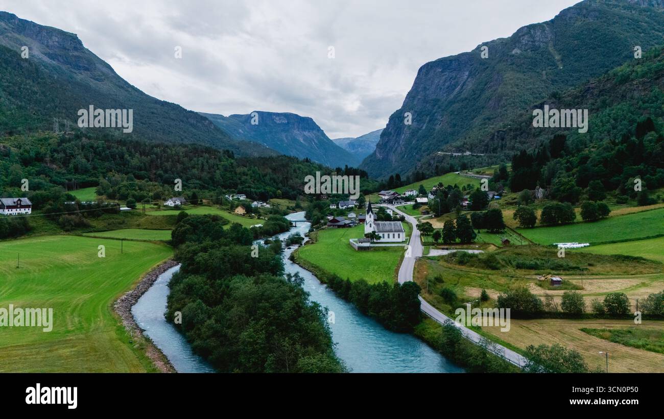 Paysage à couper le souffle de Fortun en Norvège, mettant en valeur une rivière sereine serpentant à travers des champs et des montagnes vibrants. Scène parfaite pour les amoureux de la nature et de la tranquillité au milieu de paysages magnifiques. Banque D'Images