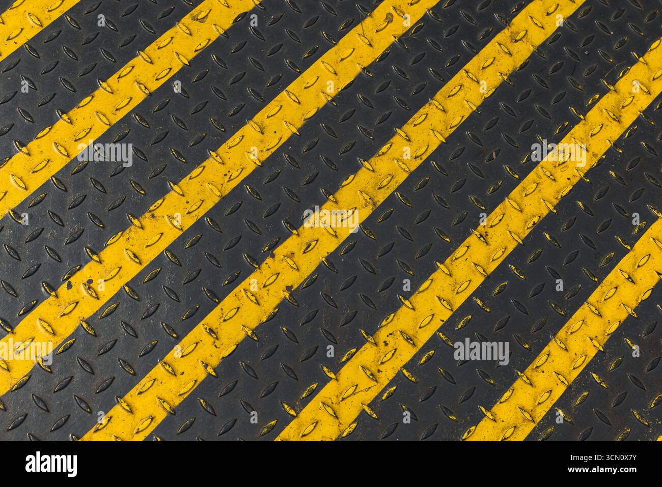 Bandes diagonales noires et jaunes industrielles peintes sur une surface métallique avec un motif antidérapant. Représente la sécurité, la prudence et le desi industriel Banque D'Images