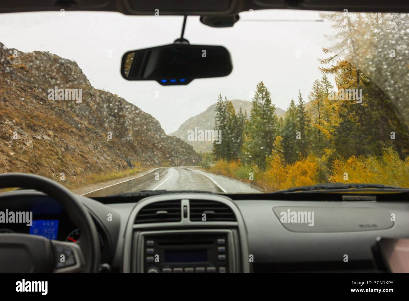A l'intérieur d'une voiture regardant à travers le pare-brise une route sinueuse dans les montagnes, entourée par la forêt d'automne et la pluie légère. Ambiance brumeuse Banque D'Images