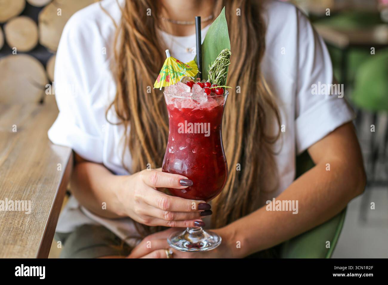 Femme tenant un cocktail d'été. Boisson rouge rafraîchissante froide avec de la glace et des fruits. Mode de vie sain des boissons en gros plan. Rafraîchissement le jour ensoleillé. Banque D'Images
