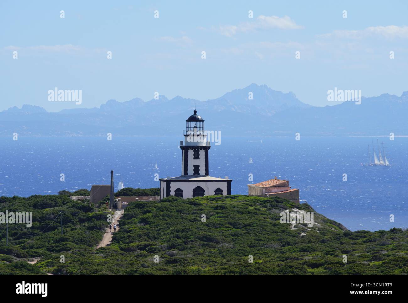 Phare côtier surplombant la mer avec voiliers et montagnes lointaines par temps clair. Bonifacio, Corse, France Banque D'Images
