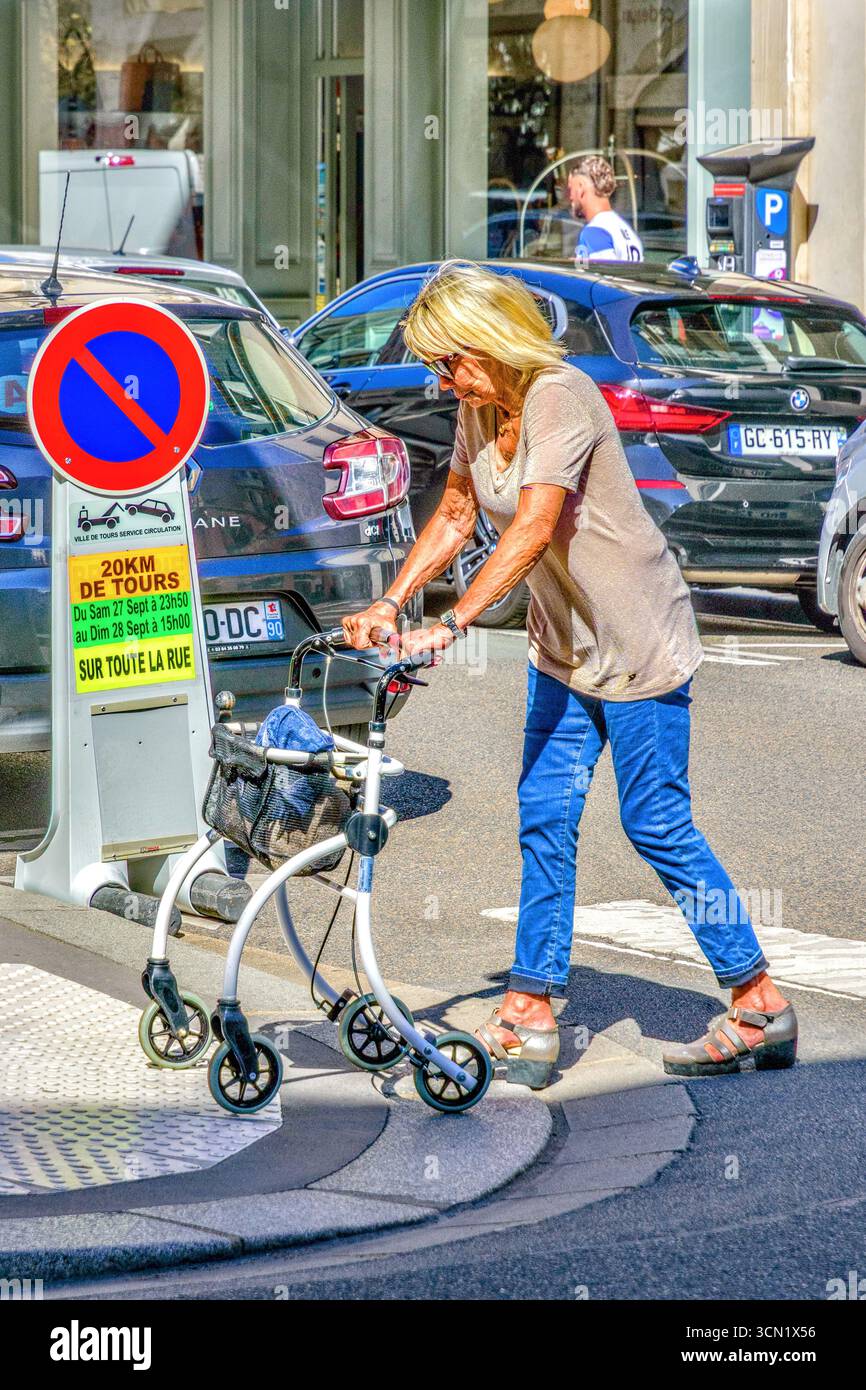 Femme infirme plus âgée, vêtue de façon décontractée, utilisant l'air de marche du rouleau pour traverser la rue de la ville - Tours, Indre-et-Loire (37), France. Banque D'Images