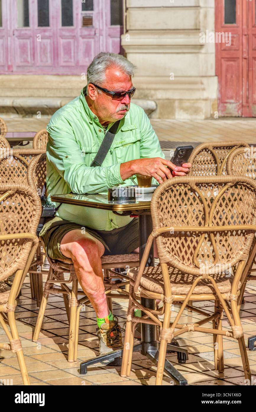 Homme avec des lunettes de soleil assis à la table de café en plein air regardant smartphone - Tours, Indre-et-Loire (37), France. Banque D'Images