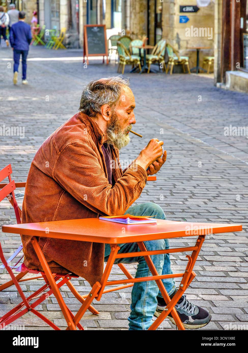 Homme barbu assis à la table de café extérieur éclairage cheroot - Tours, Indre-et-Loire (37), France. Banque D'Images