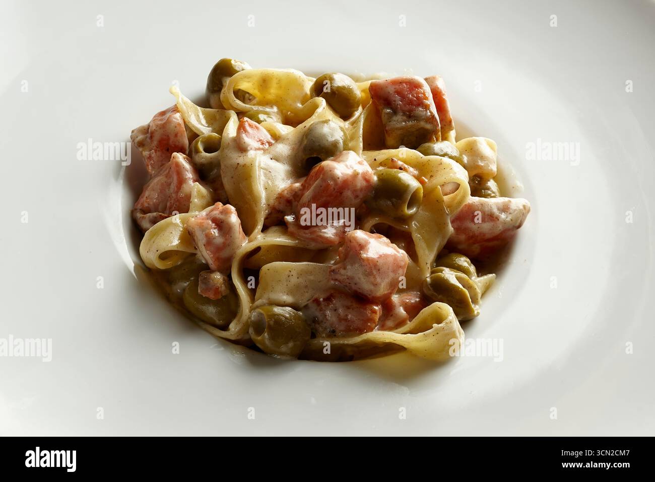 Gros plan de pâtes avec sauce aux champignons crémeux et jambon sur une assiette blanche ordinaire avec espace de copie. Conçu pour la photographie de stock de nourriture et la conception de menus. Banque D'Images