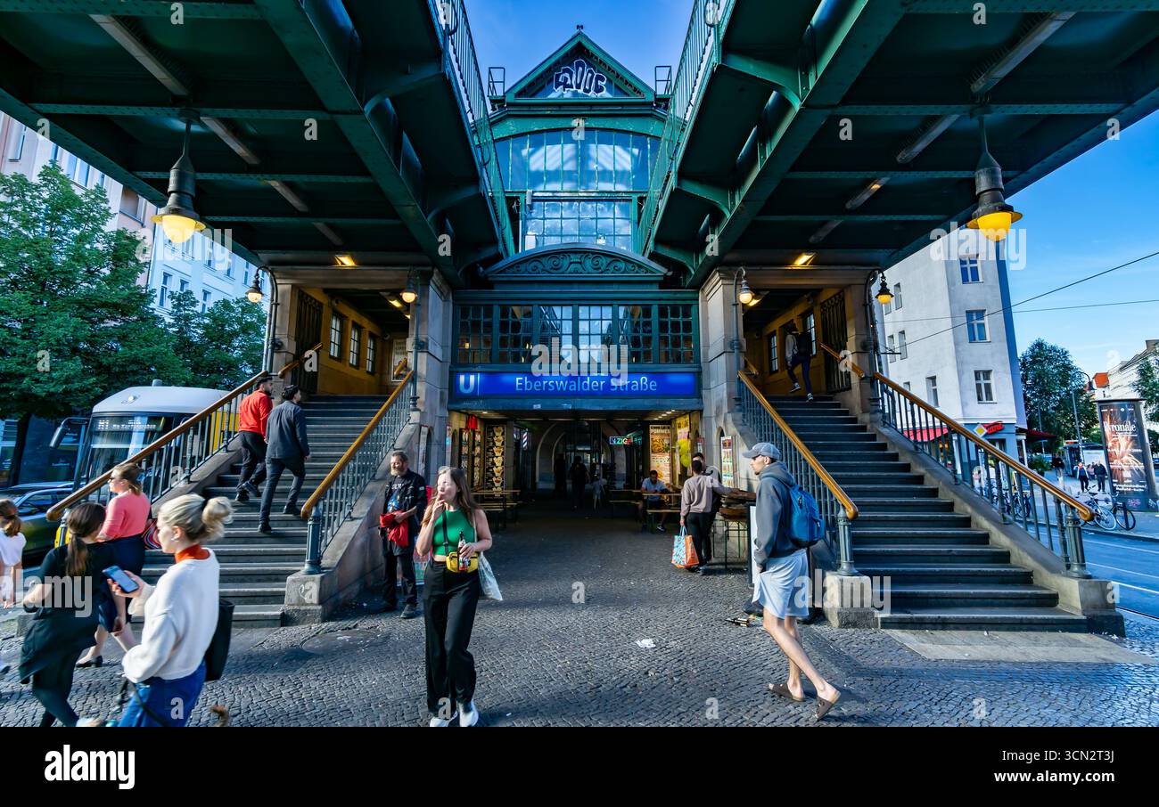 Vue de face de l'entrée du U-Bahn Eberswalder Straße sous des voies surélevées avec des gens marchant et l'atmosphère de la ville en soirée. Banque D'Images