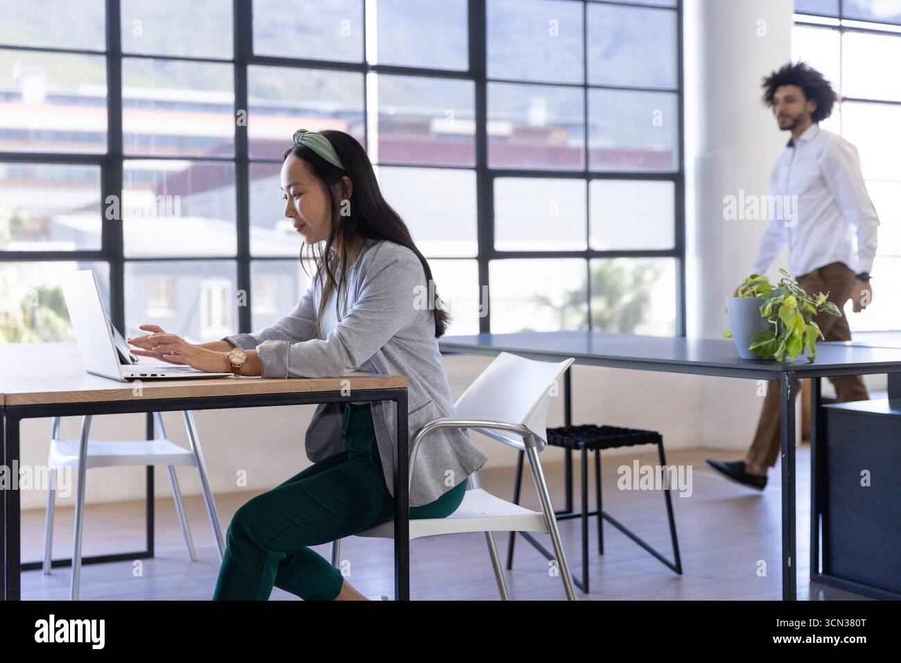 Les ordinateurs portables sont assis sur des bureaux en bois tandis que les chaises blanches encadrent les fenêtres grillagées dans le bureau Banque D'Images