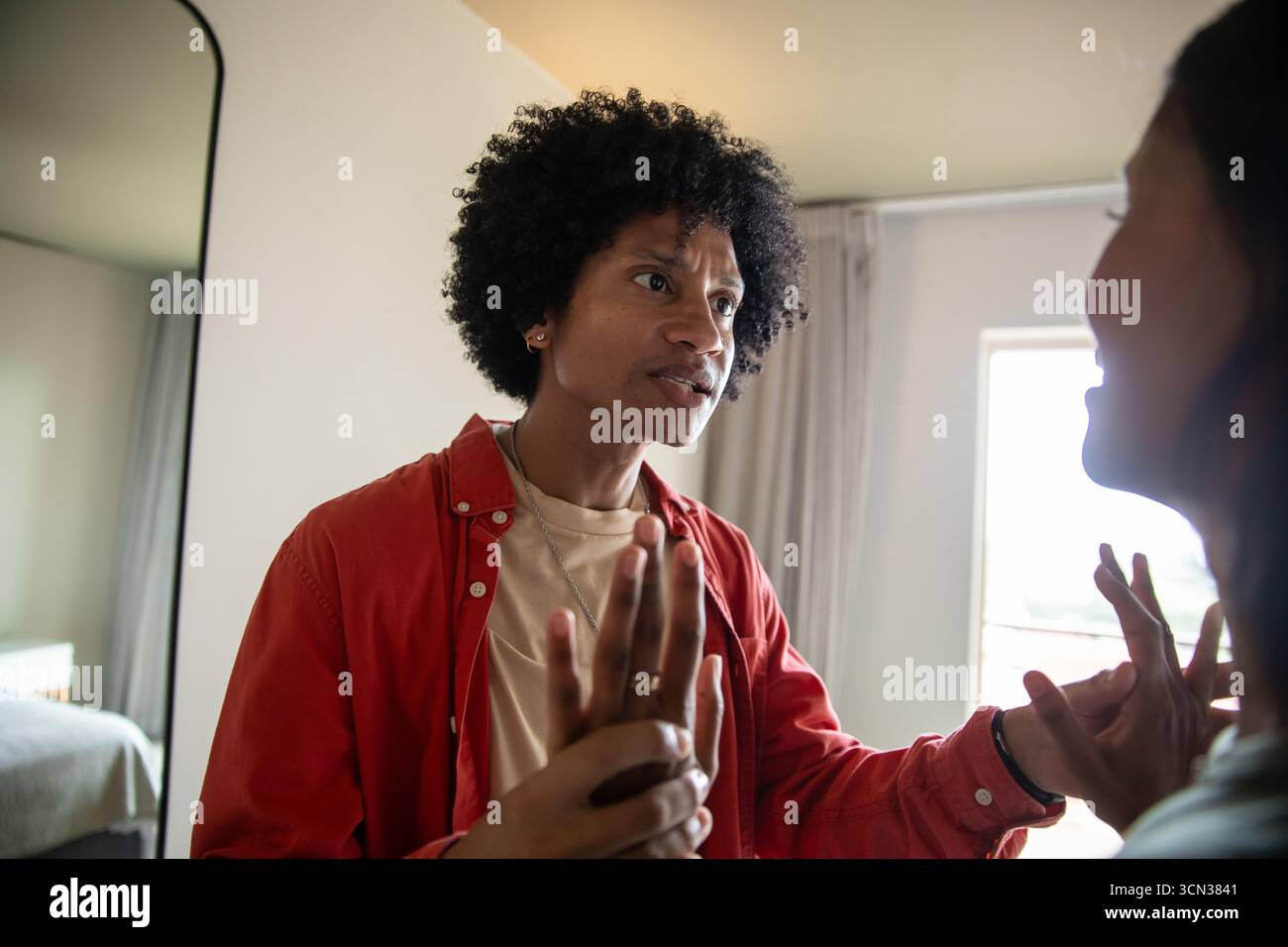 Couple tenant les mains ensemble au niveau de la poitrine dans la chambre près du miroir mural, fenêtre Banque D'Images Couple tenant les mains ensemble au niveau de la poitrine dans la chambre près du miroir mural, fenêtre Banque D'Images