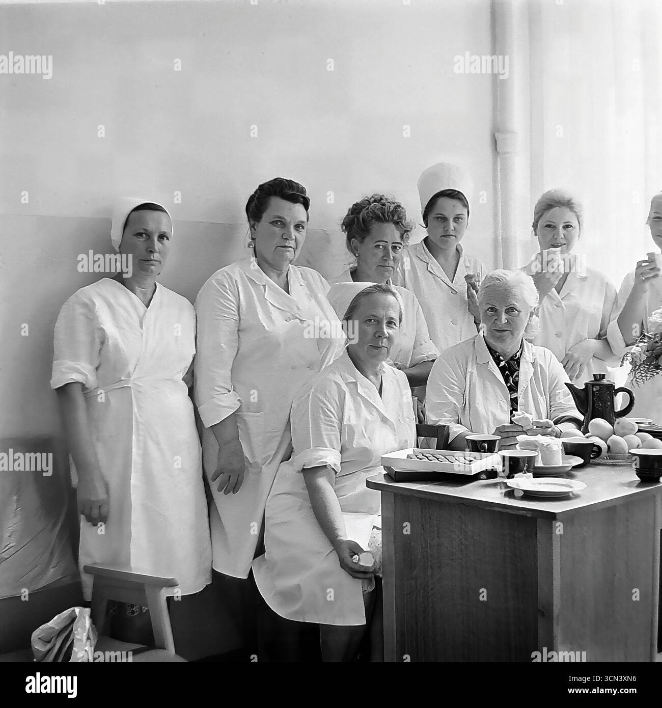 Portrait de groupe historique des années 1970-80, montrant un collectif de travail féminin d'une cantine ou d'une unité de restauration à la station balnéaire de Slavkurort, RSS d'Ukraine. Les employés, cuisiniers et cuisiniers, en uniformes blancs et casquettes, sont réunis à une table lors d’une pause ou d’une petite fête. L'image est un document authentique reflétant le travail quotidien et la vie des travailleurs de la restauration publique en URSS Banque D'Images