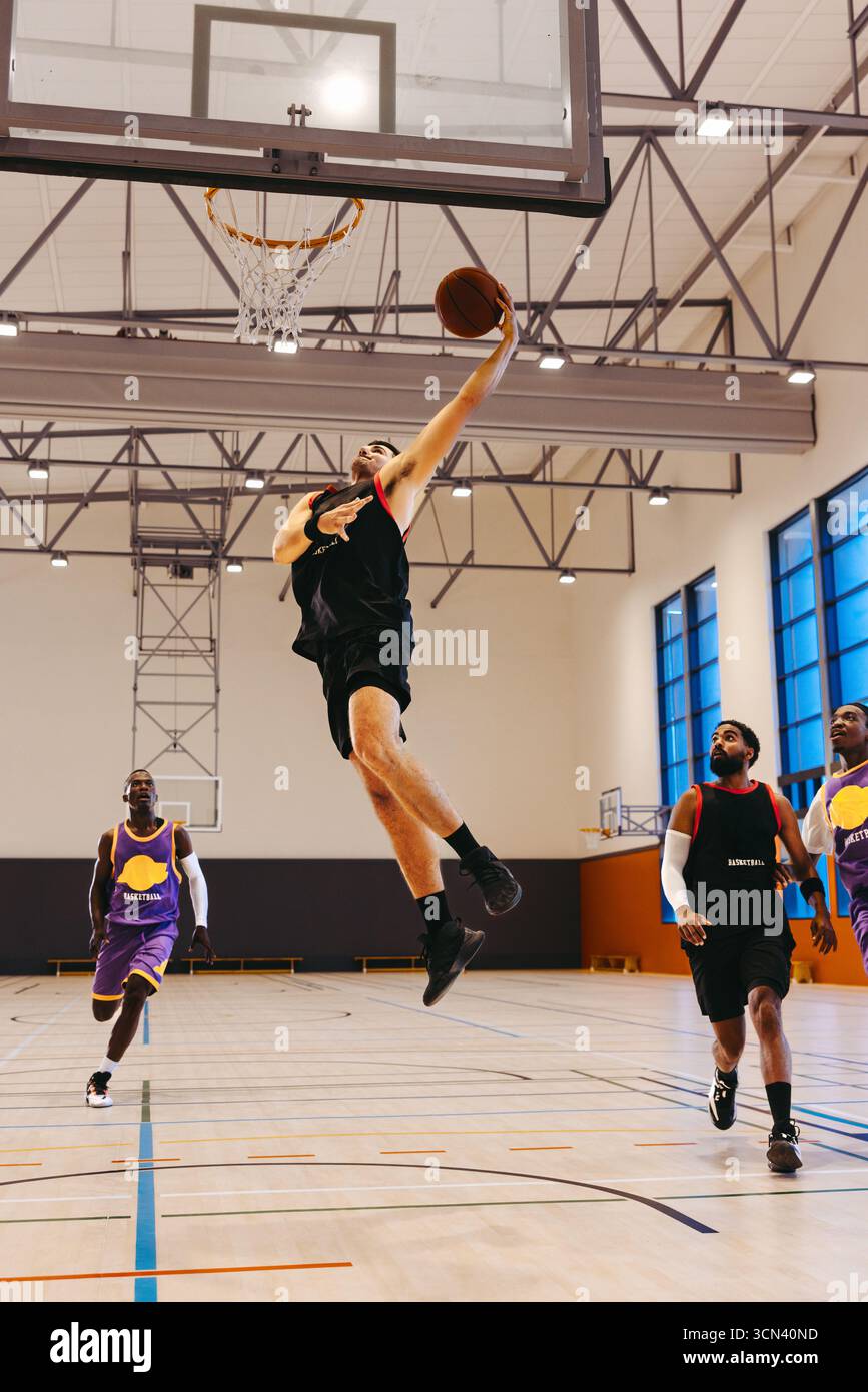 Match de basket-ball dynamique entre quatre jeunes hommes sur un terrain, avec un joueur en plein air tentant un panier tandis que d'autres s'affrontent activement dans la haute humeur Banque D'Images Match de basket-ball dynamique entre quatre jeunes hommes sur un terrain, avec un joueur en plein air tentant un panier tandis que d'autres s'affrontent activement dans la haute humeur Banque D'Images