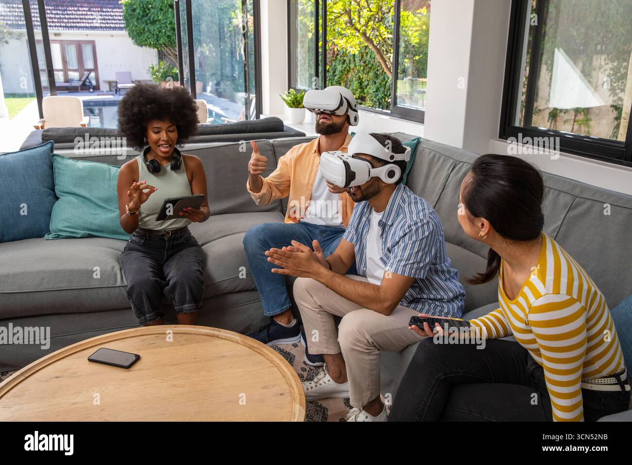 Divers amis jouant à des jeux de réalité virtuelle dans le salon sur le canapé avec tablette A. Banque D'Images
