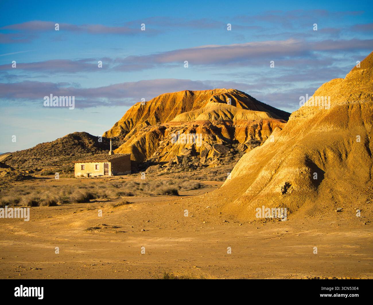 Petite maison dans le désert de Bardenas Reales au coucher du soleil - paysage aride avec une habitation solitaire en adobe sous la lumière dorée et un ciel dramatique. Banque D'Images
